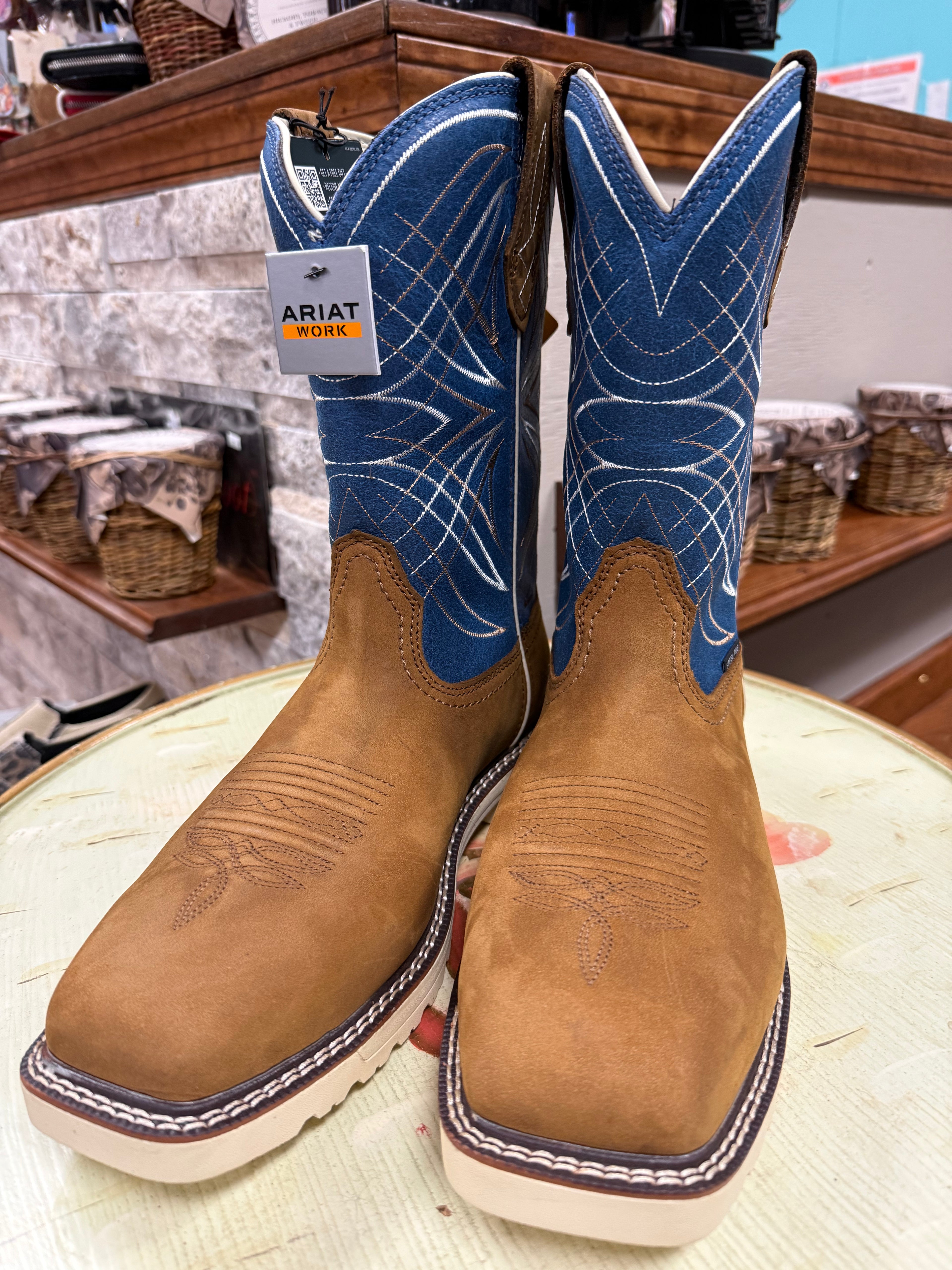 Pair of Ariat cowboy boots with blue uppers and brown shafts on a wooden surface.