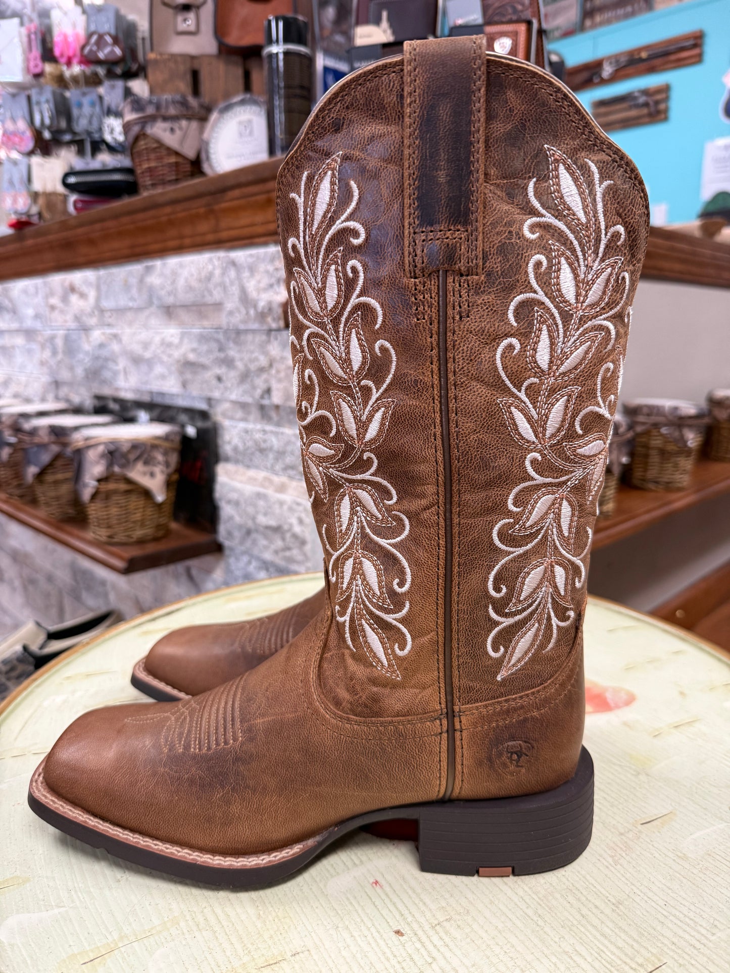 Brown cowboy boot with white embroidery on a wooden surface.