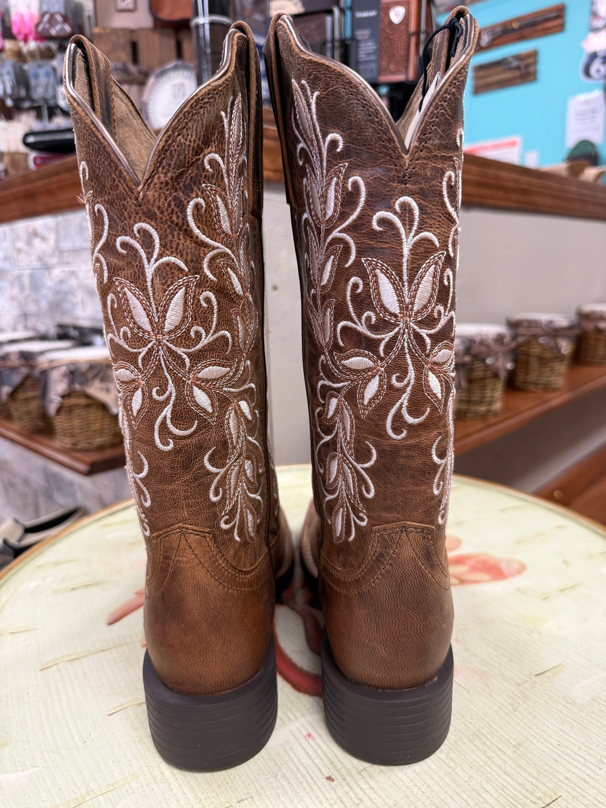 Pair of brown cowboy boots with white embroidery on a round surface.