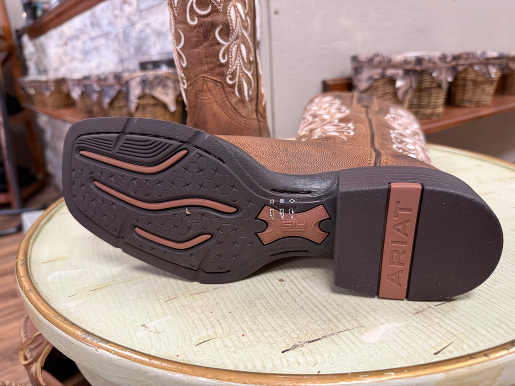 Brown Ariat cowboy boot with a focus on the sole on a light green surface.