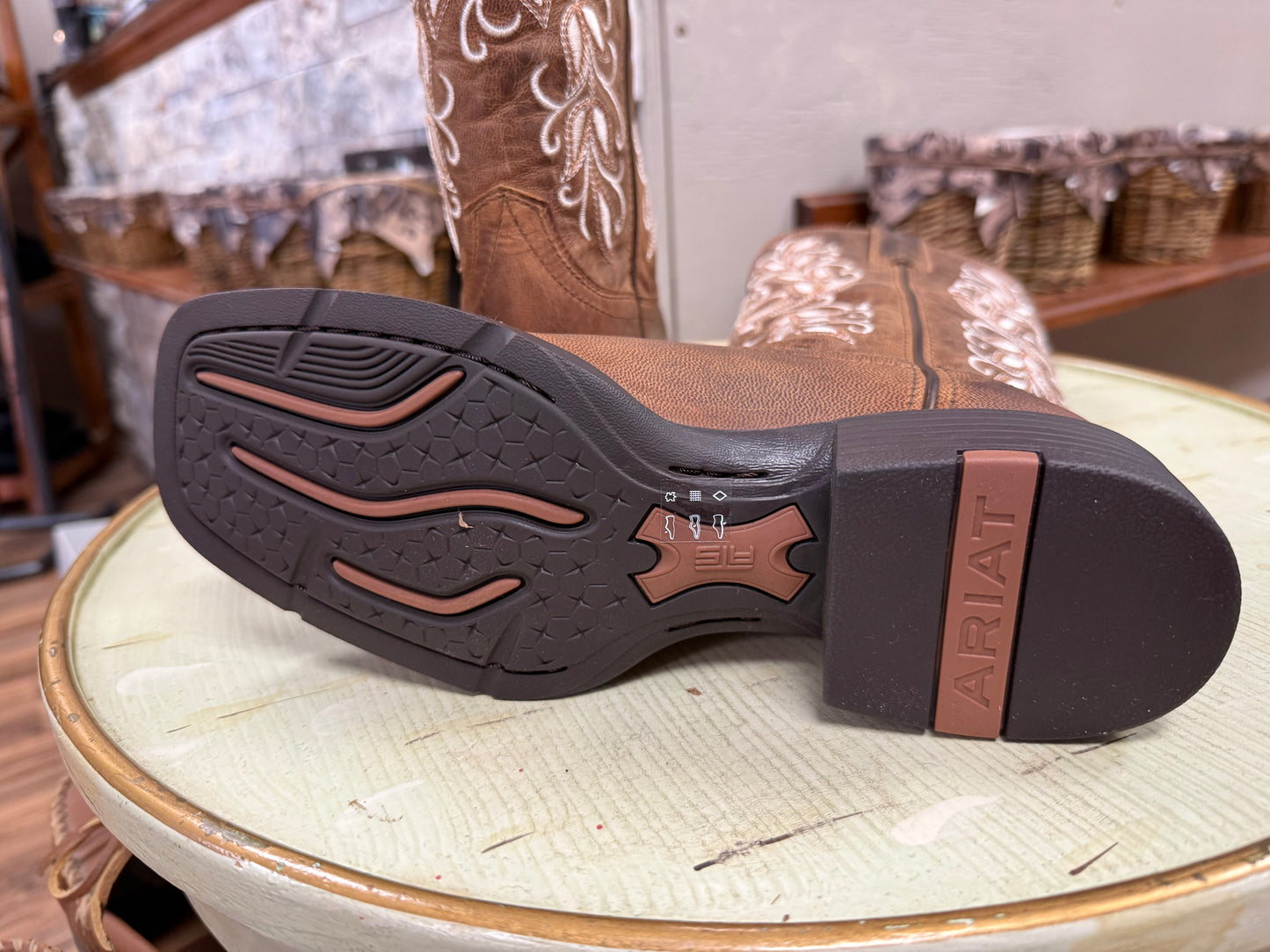 Brown Ariat cowboy boot with a focus on the sole on a light green surface.