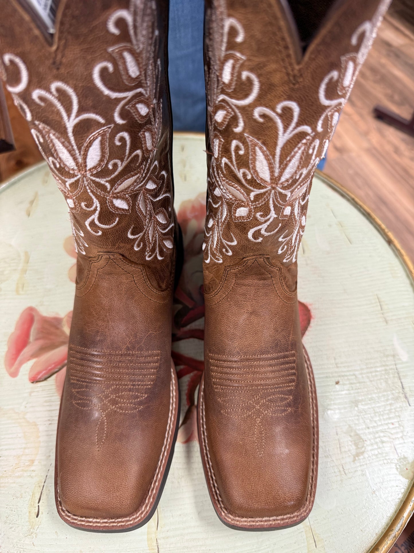 Brown cowboy boots with intricate white embroidery on a wooden surface.