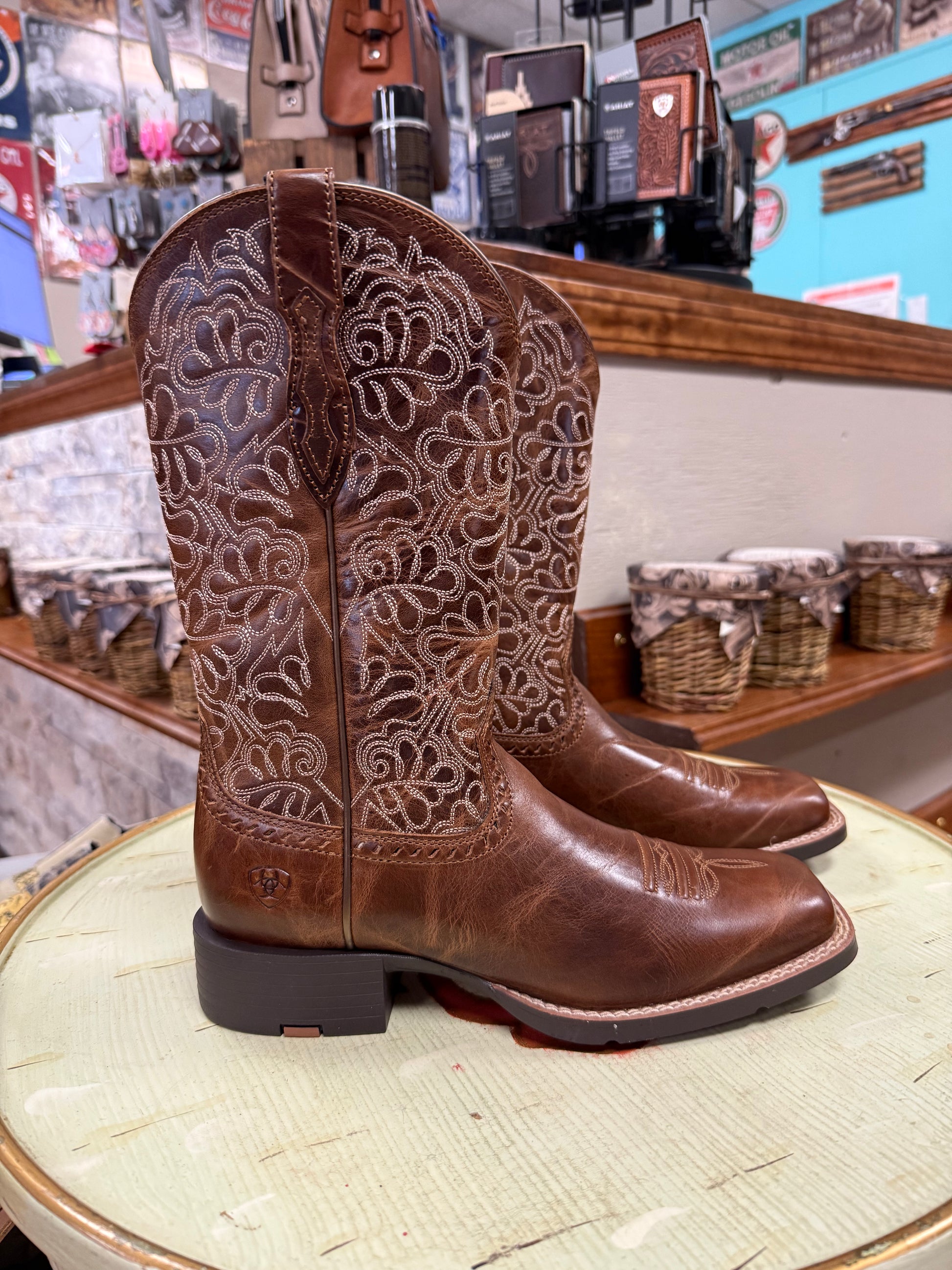 Brown cowboy boots with intricate patterns on a round surface in a store setting.