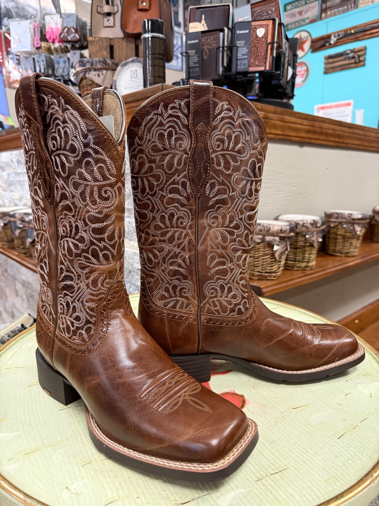 Pair of brown cowboy boots with intricate patterns on a display table.