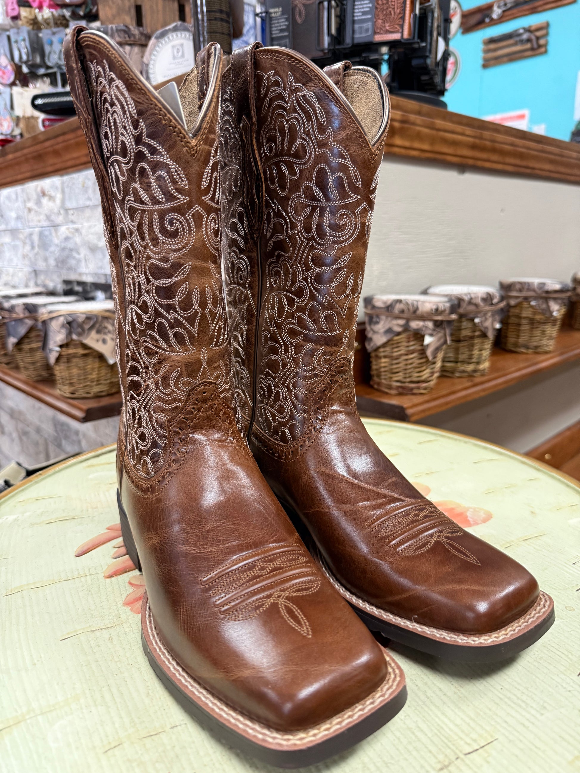 Pair of brown cowboy boots with intricate patterns on a light green surface.