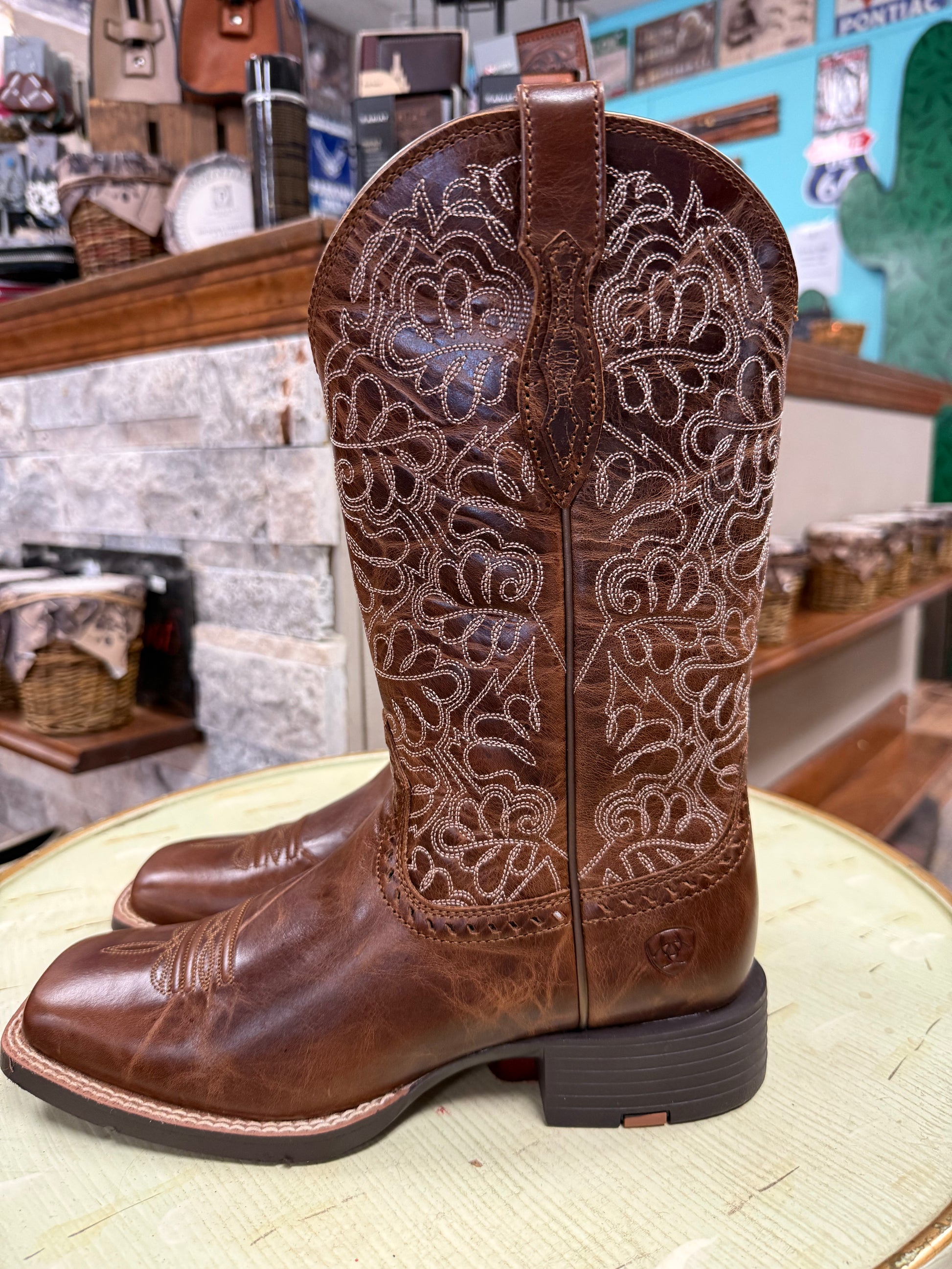 Brown cowboy boots with intricate white embroidery on a textured surface.