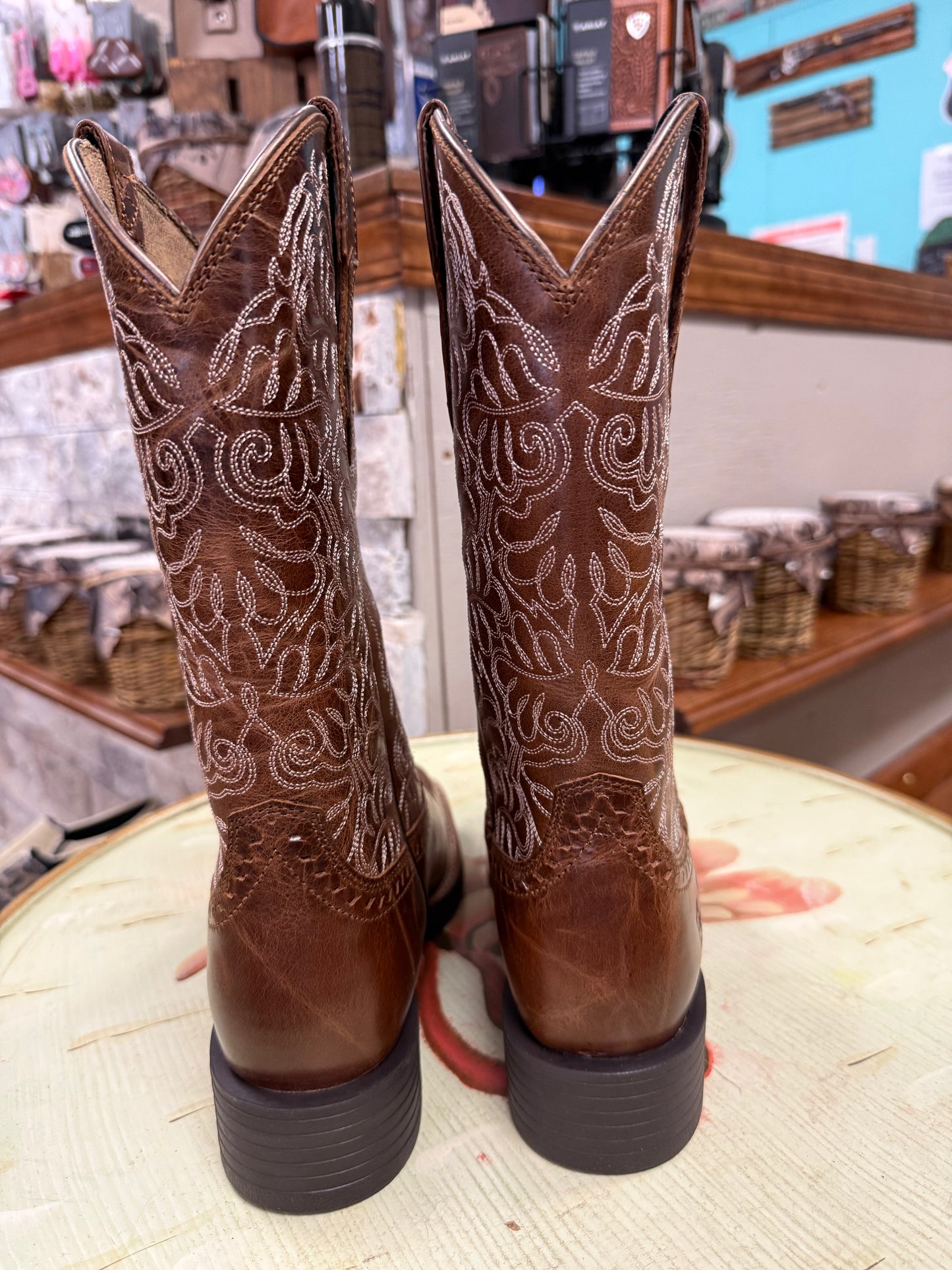 Pair of brown cowboy boots with intricate white patterns on a round surface.