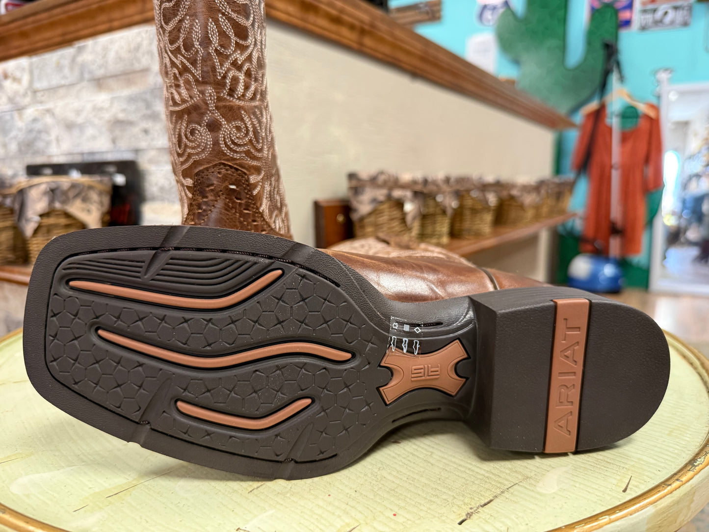 Close-up of a cowboy boot sole with 'Ariat' branding in a store setting.