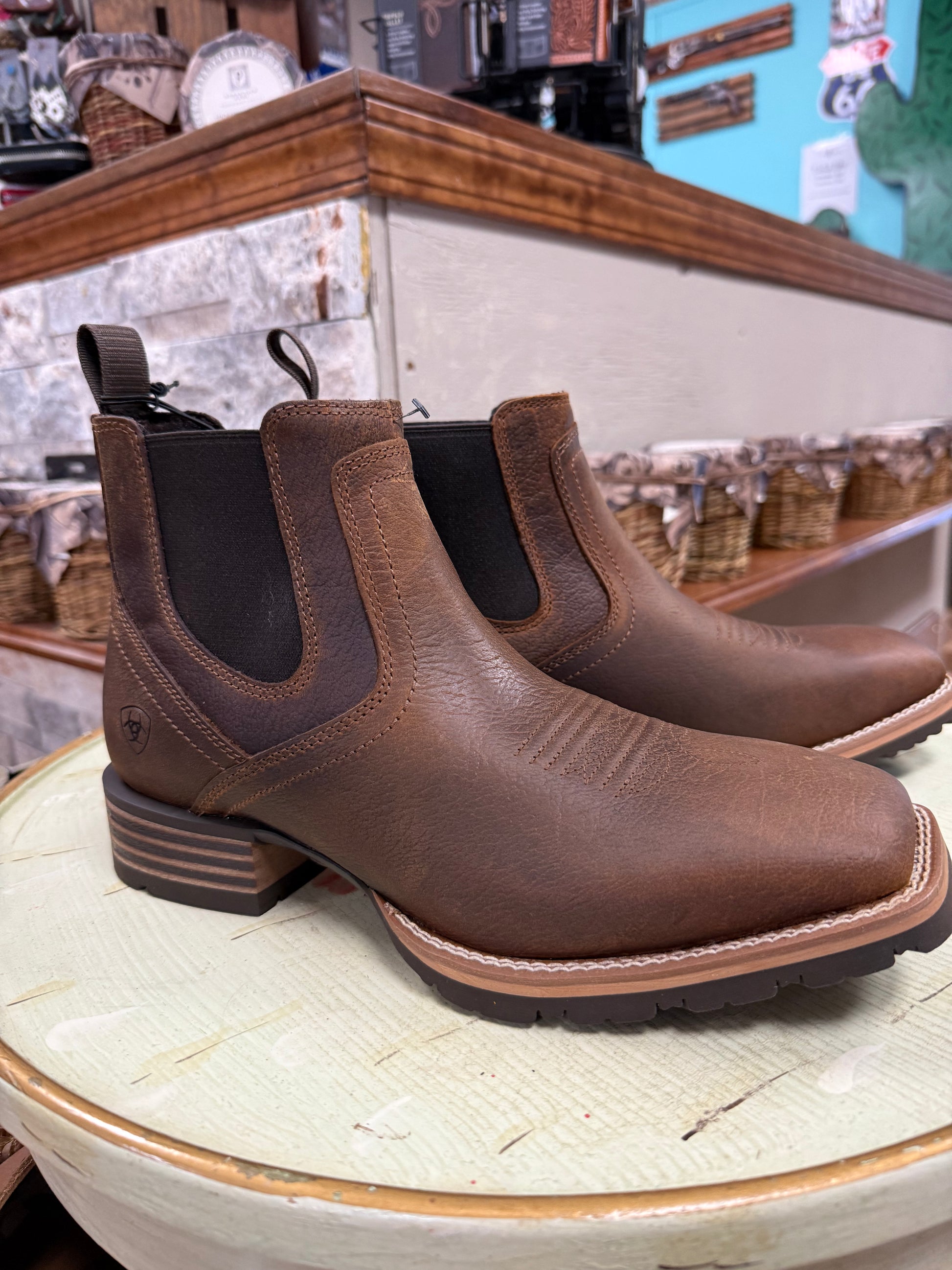 Brown leather boots on a wooden surface with a store setting in the background