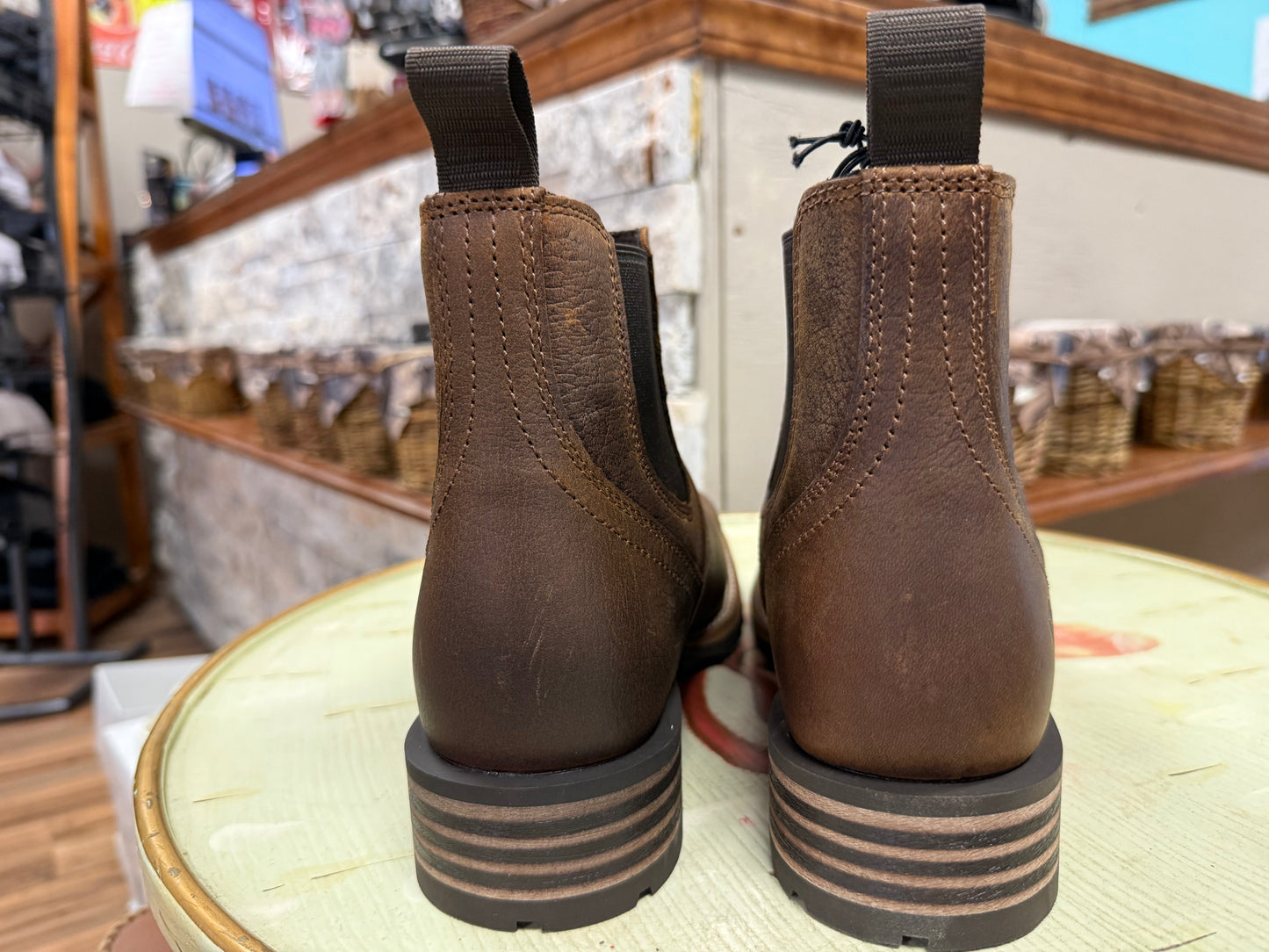 Pair of brown leather boots on a wooden stool with a store interior background.