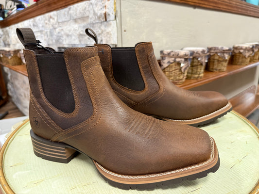 Pair of brown leather boots on a wooden surface with a store shelf in the background.