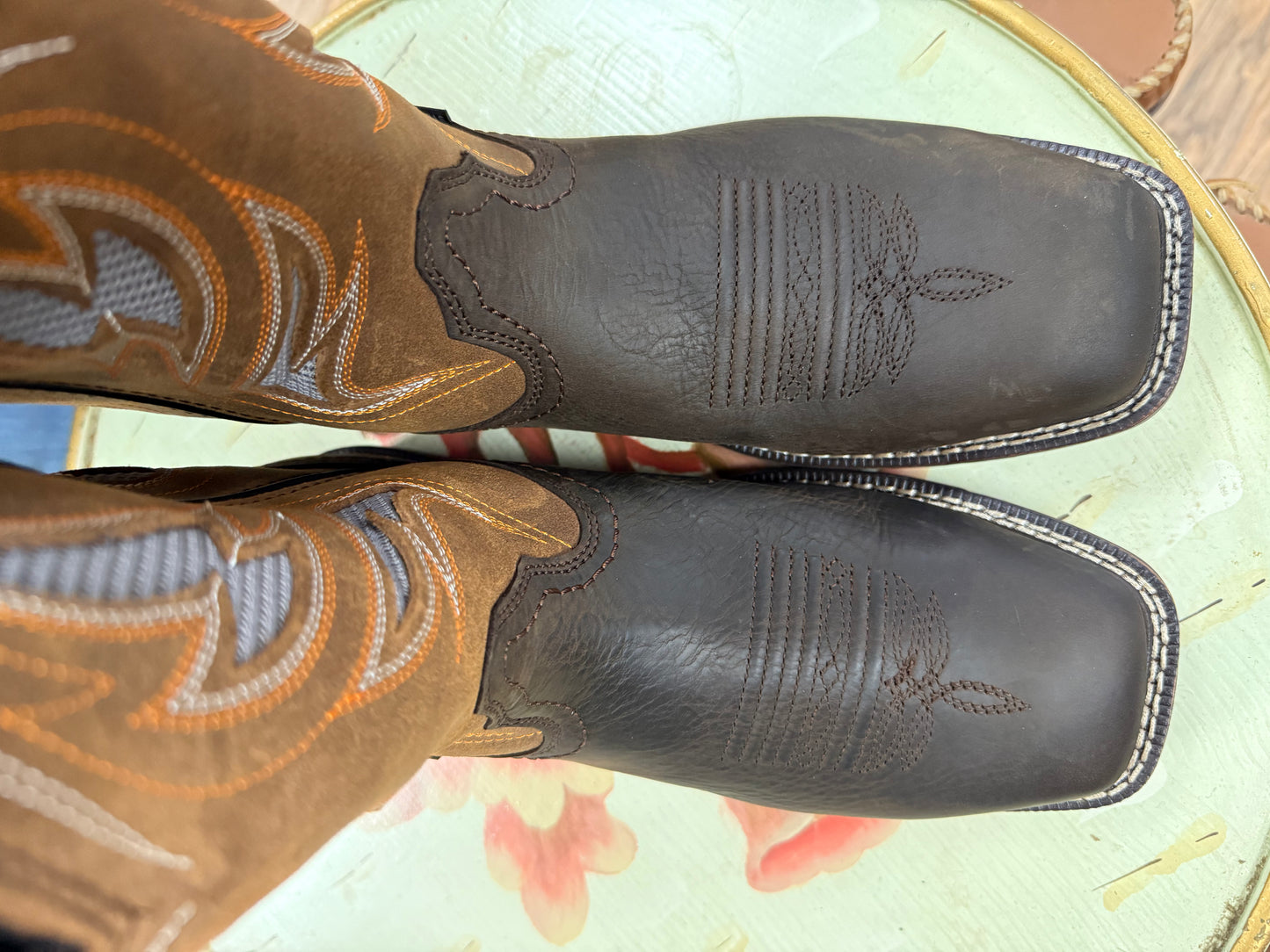 Pair of brown leather cowboy boots with intricate designs on a floral surface.