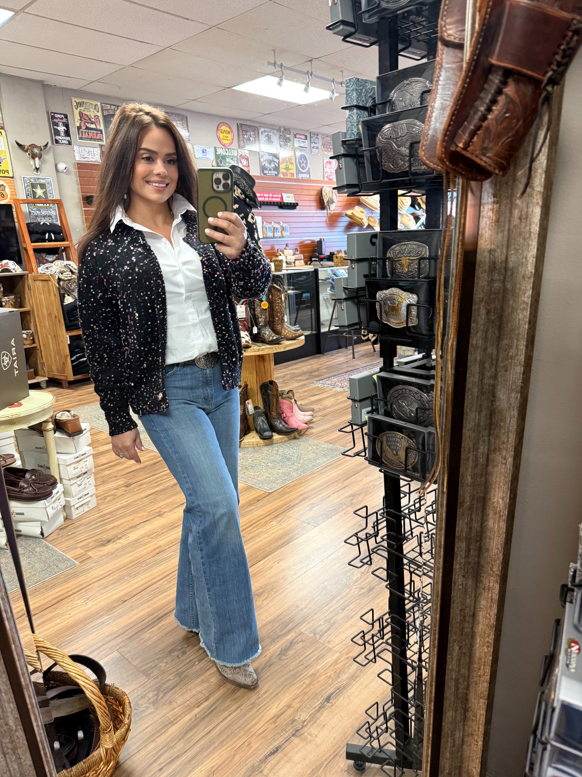 Woman taking a mirror selfie in a store with boots and decor on display.