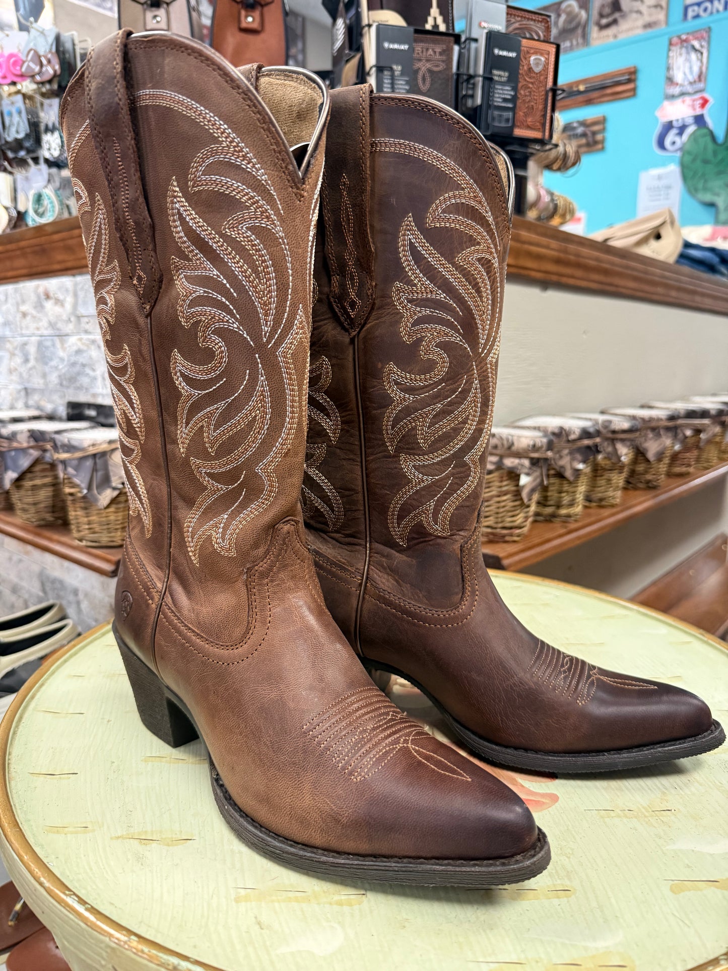 Pair of brown cowboy boots on a round table with a store interior background