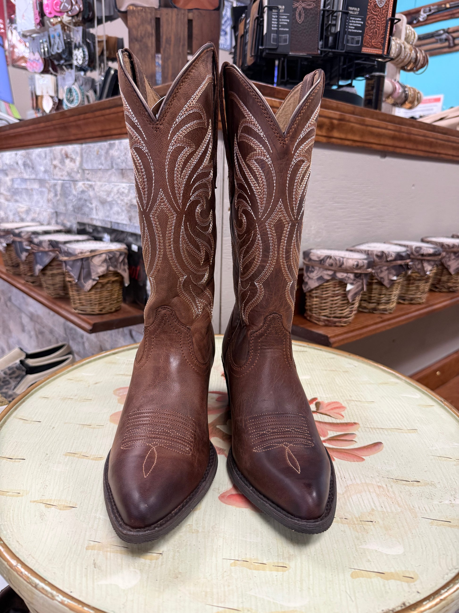 Pair of brown cowboy boots on a decorative table with a store setting in the background