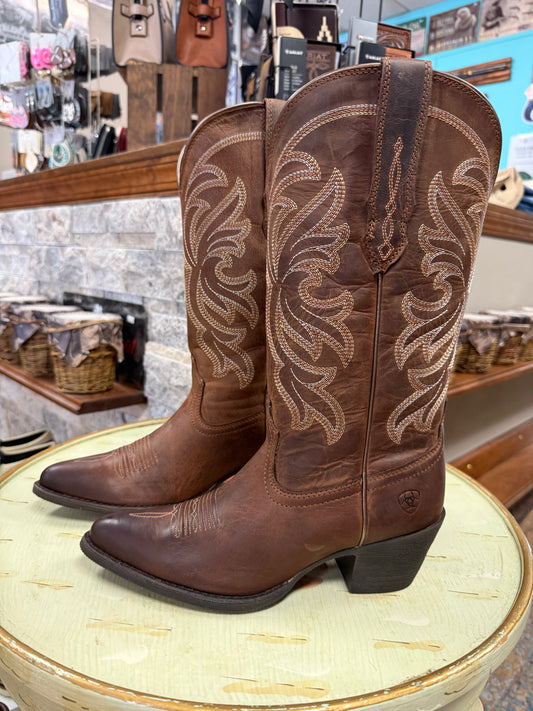 Brown cowboy boots with intricate designs on a round surface in a store setting.