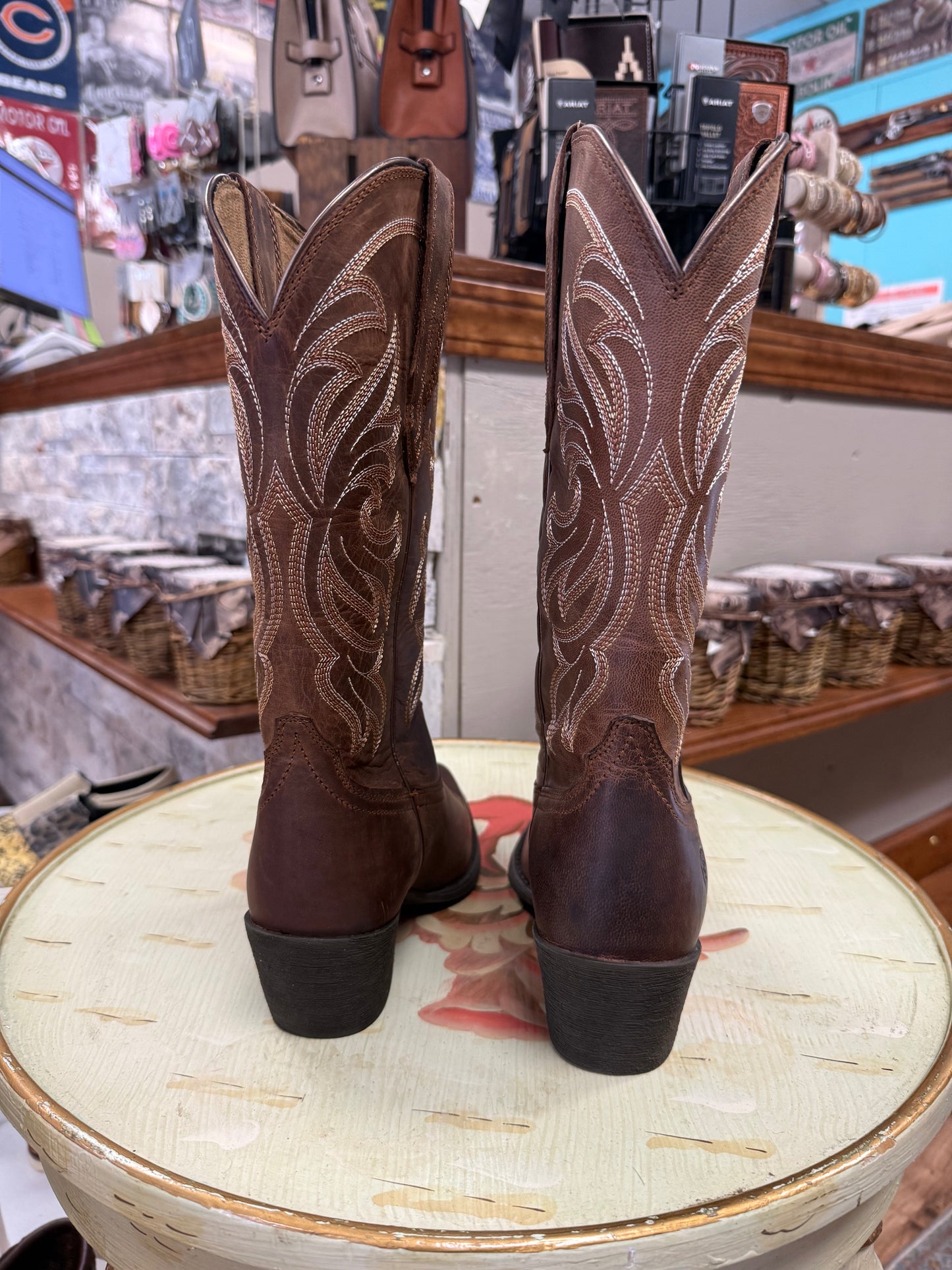 Brown cowboy boots with intricate designs on a round surface in a store setting.