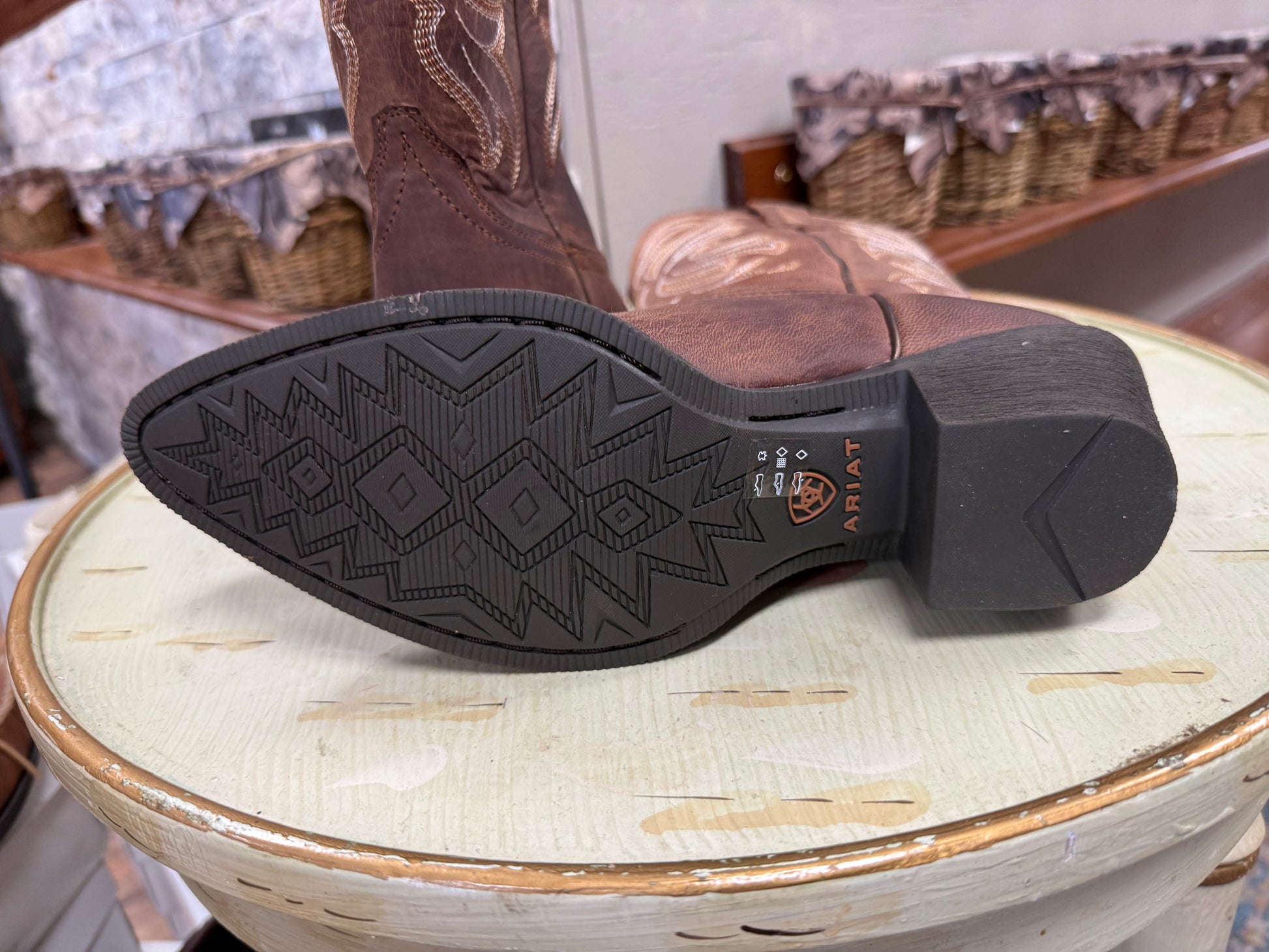Brown cowboy boot with a patterned sole on a wooden stool.