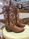 Brown cowboy boots with floral embroidery on a round surface in a store setting.