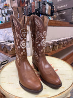 Pair of brown Ariat cowboy boots with floral patterns on a round surface in a store setting.