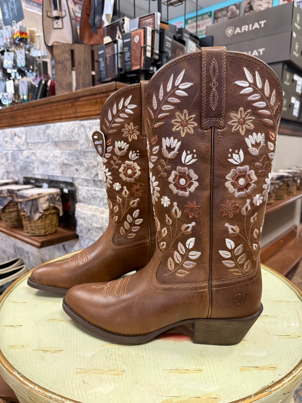 Brown cowboy boots with floral embroidery on a round surface in a store setting.