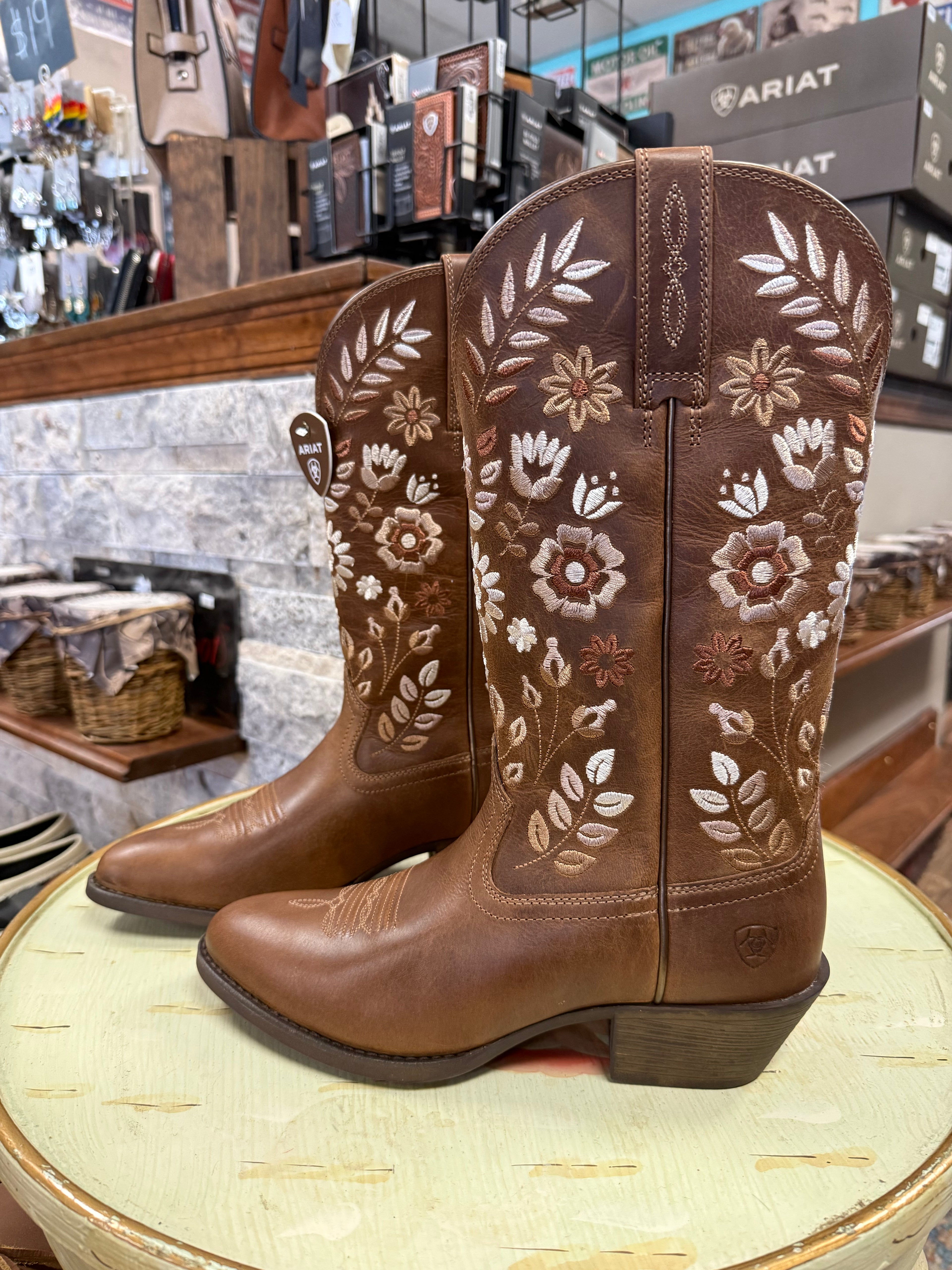 Brown cowboy boots with floral embroidery on a round surface in a store setting.