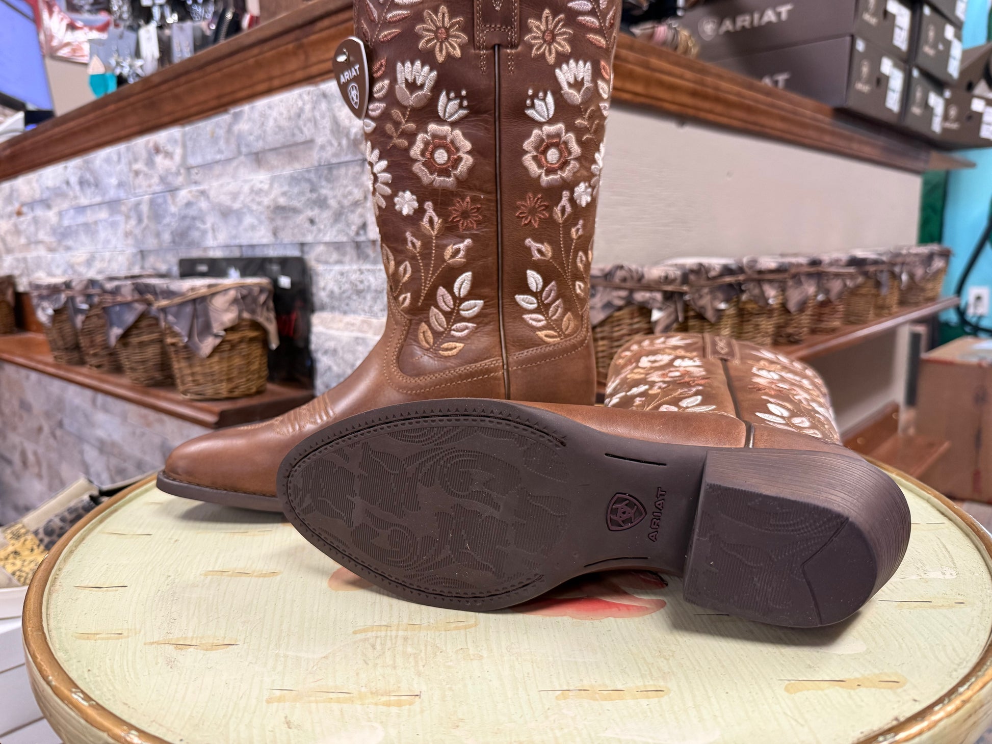 Brown cowboy boots with floral patterns on a round surface in a store setting.