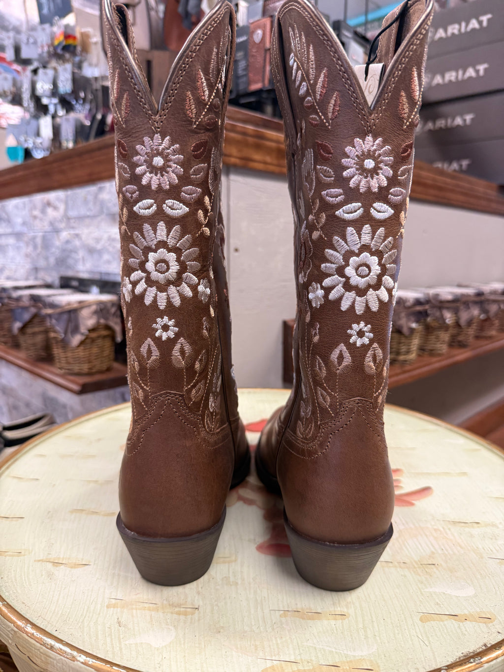 Brown cowboy boots with floral patterns on a round surface in a store setting.