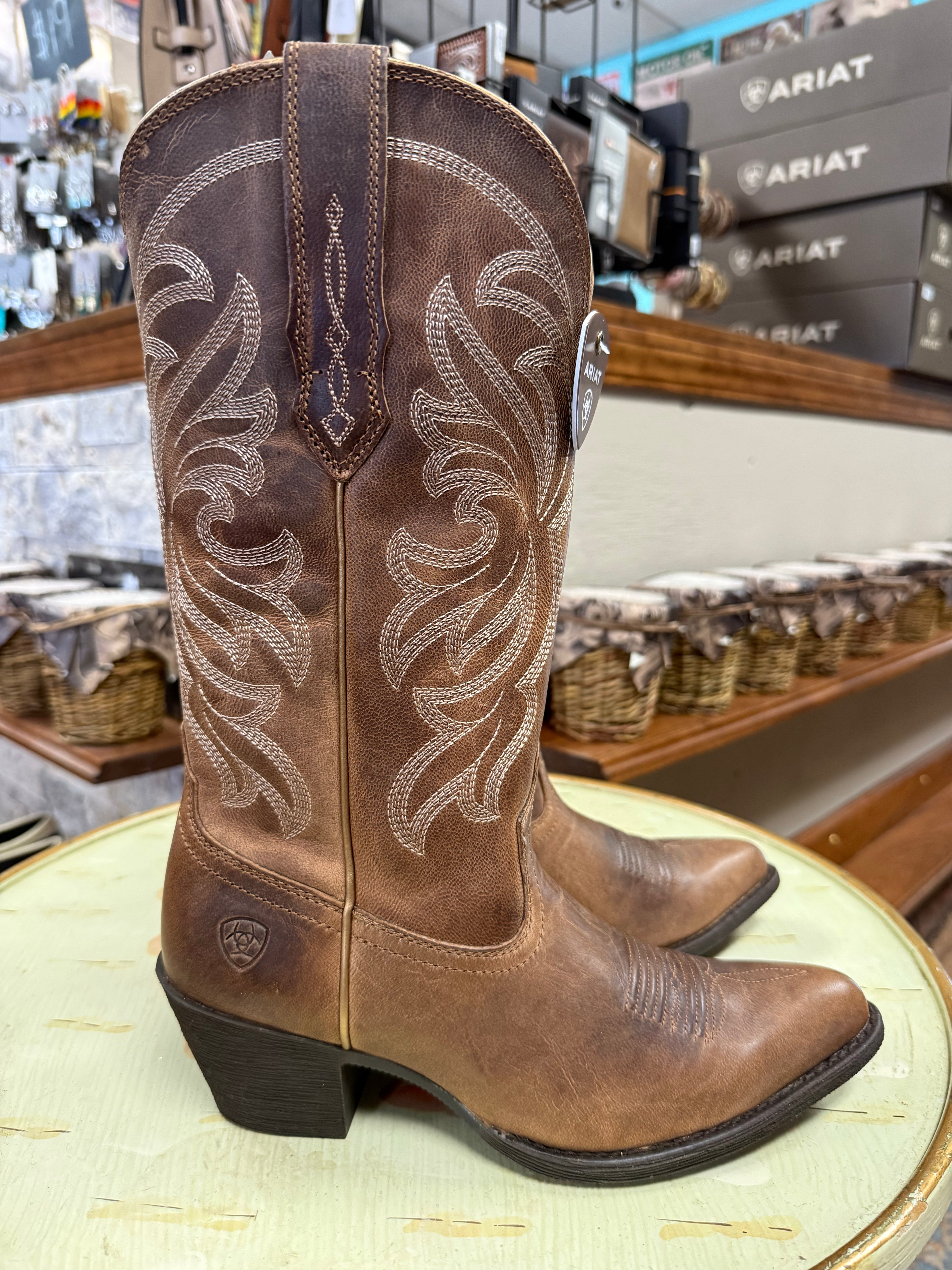 Brown cowboy boots with intricate designs on a round surface, with a store setting in the background.