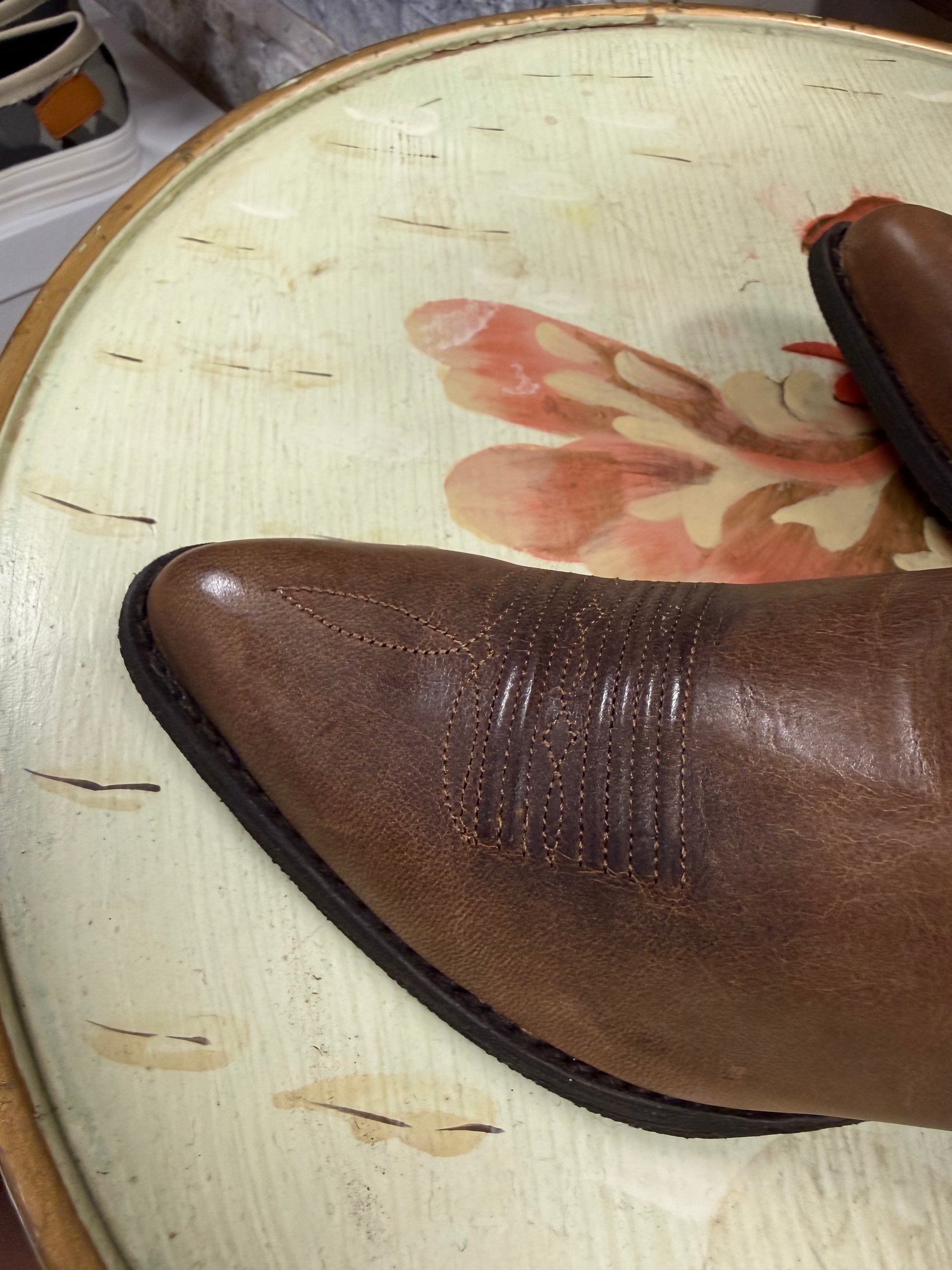 Brown leather boot on a textured surface with floral design