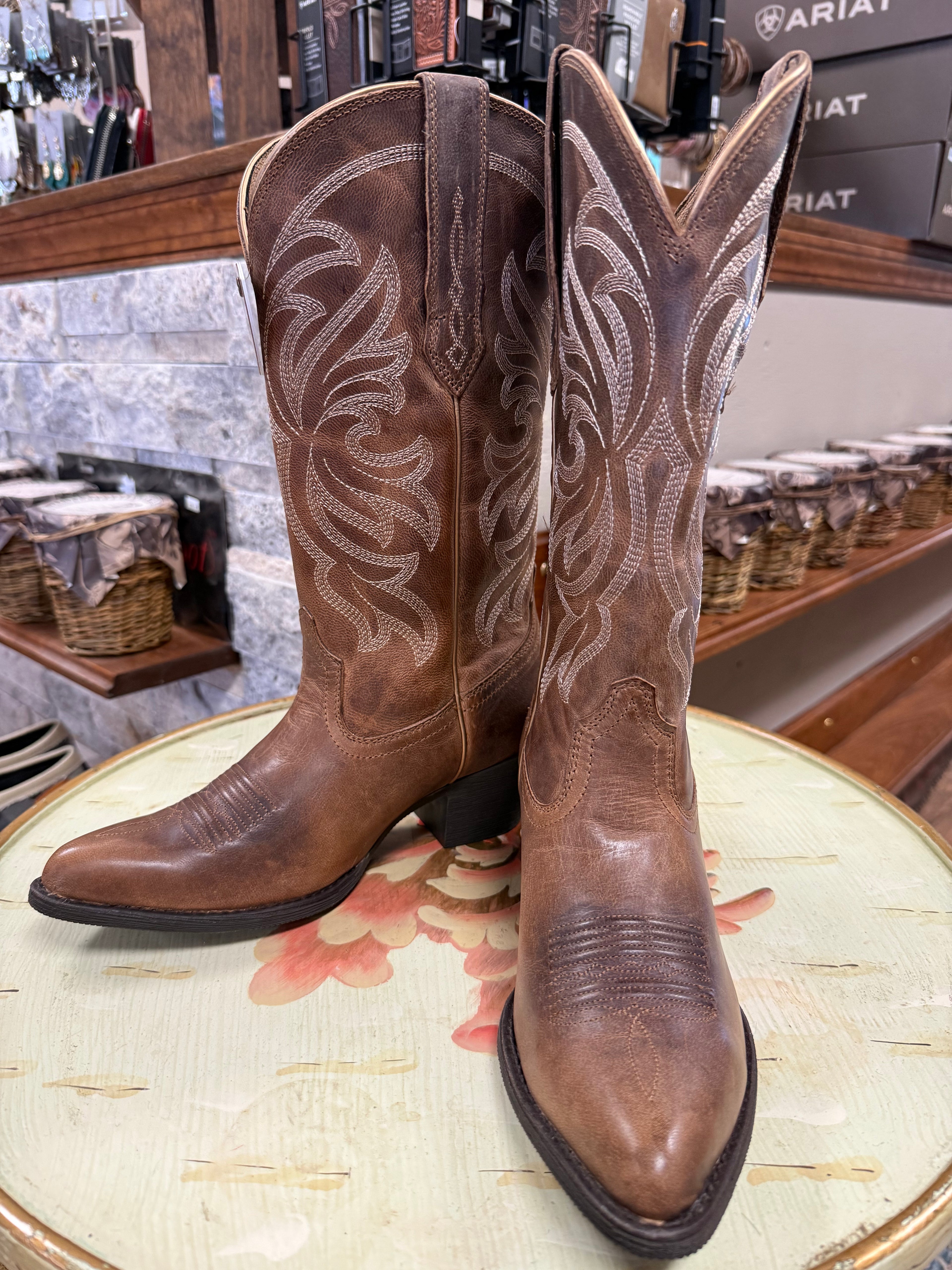 Pair of brown cowboy boots with intricate designs on a floral-patterned surface.