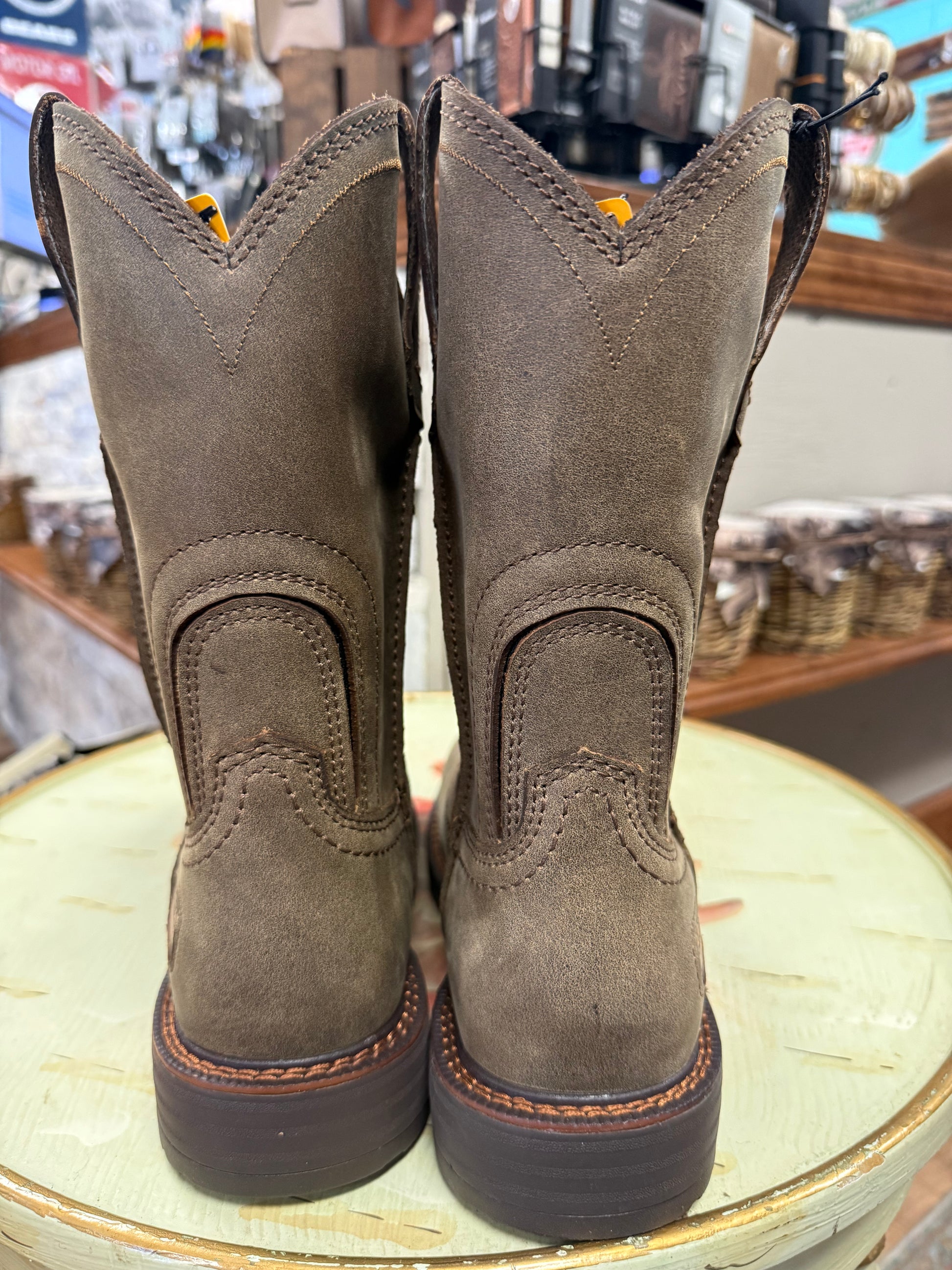 Pair of brown leather boots on a round surface with a store setting in the background.