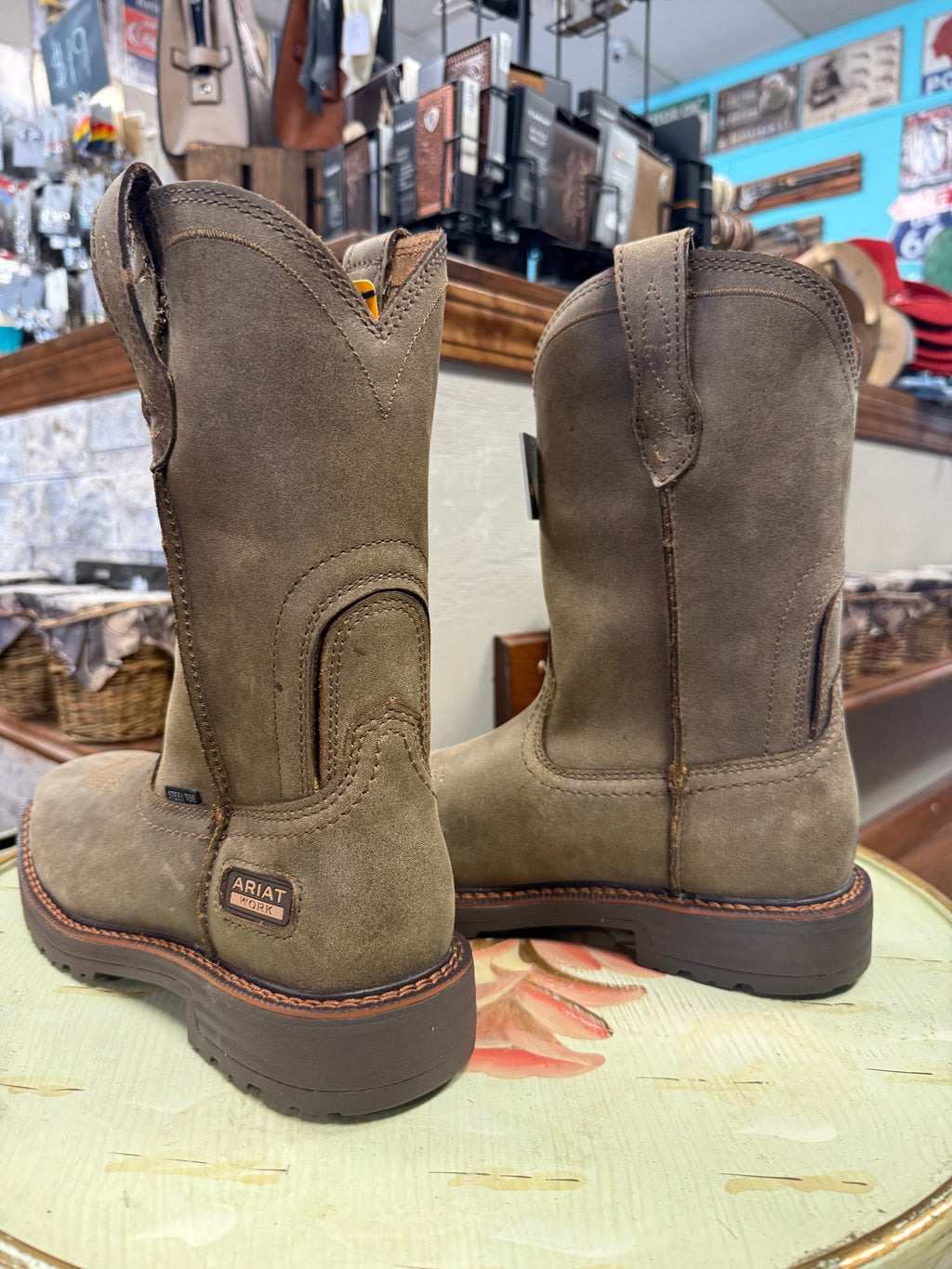 Pair of brown Ariat boots on a store display with various products in the background.