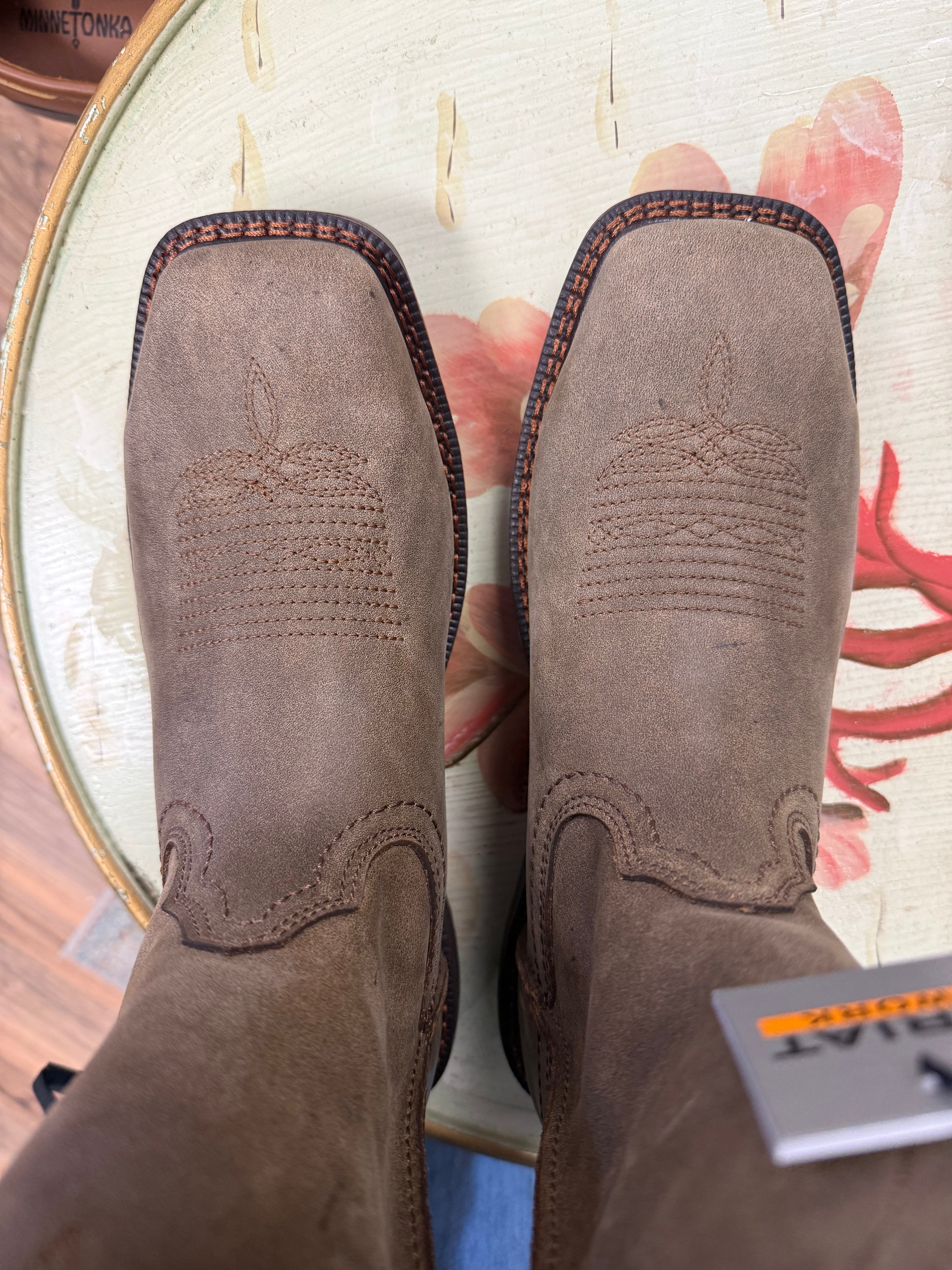 Brown leather boots with intricate stitching on a colorful background