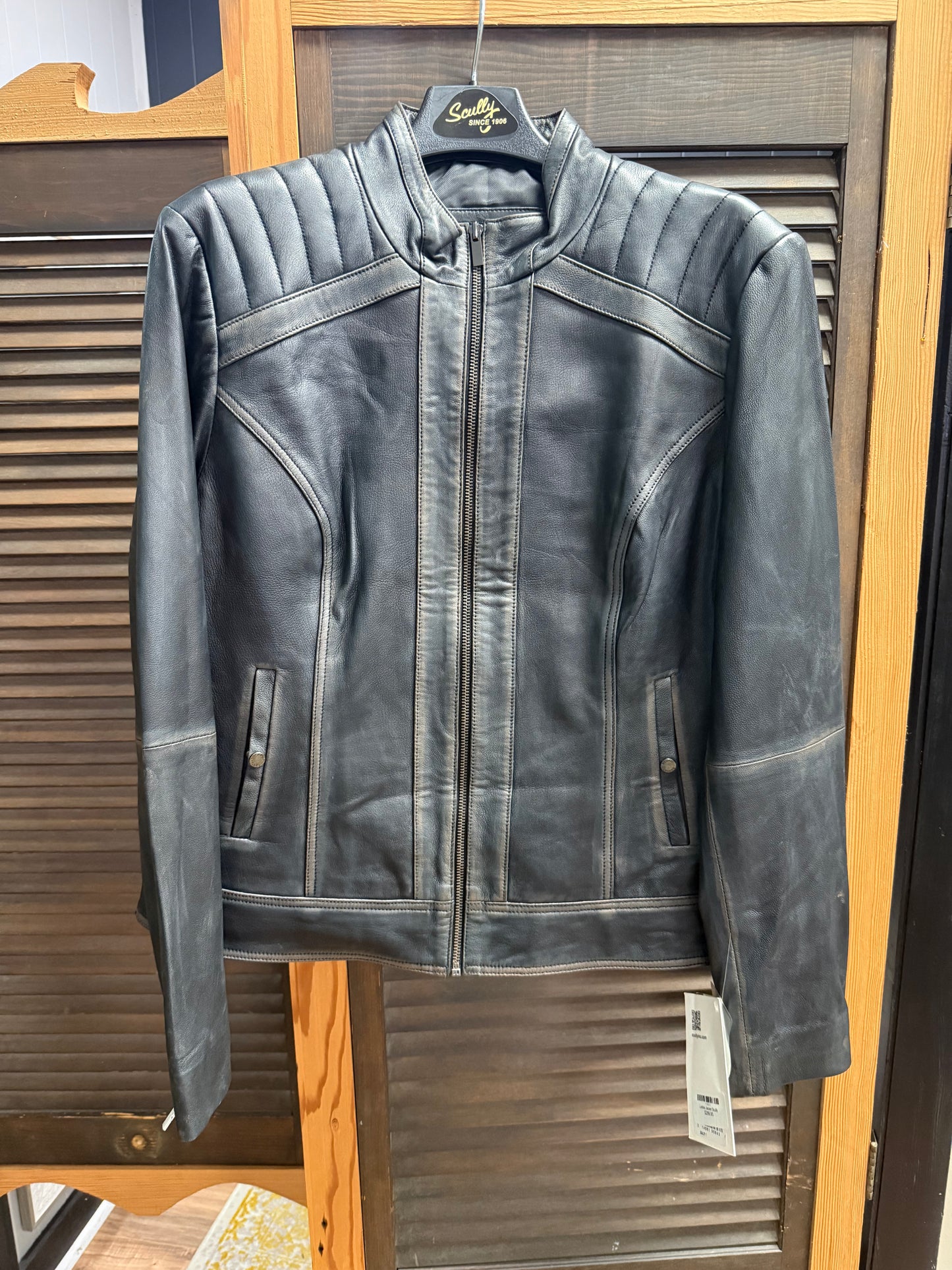 Black leather jacket on a hanger with a visible brand tag against a wooden background