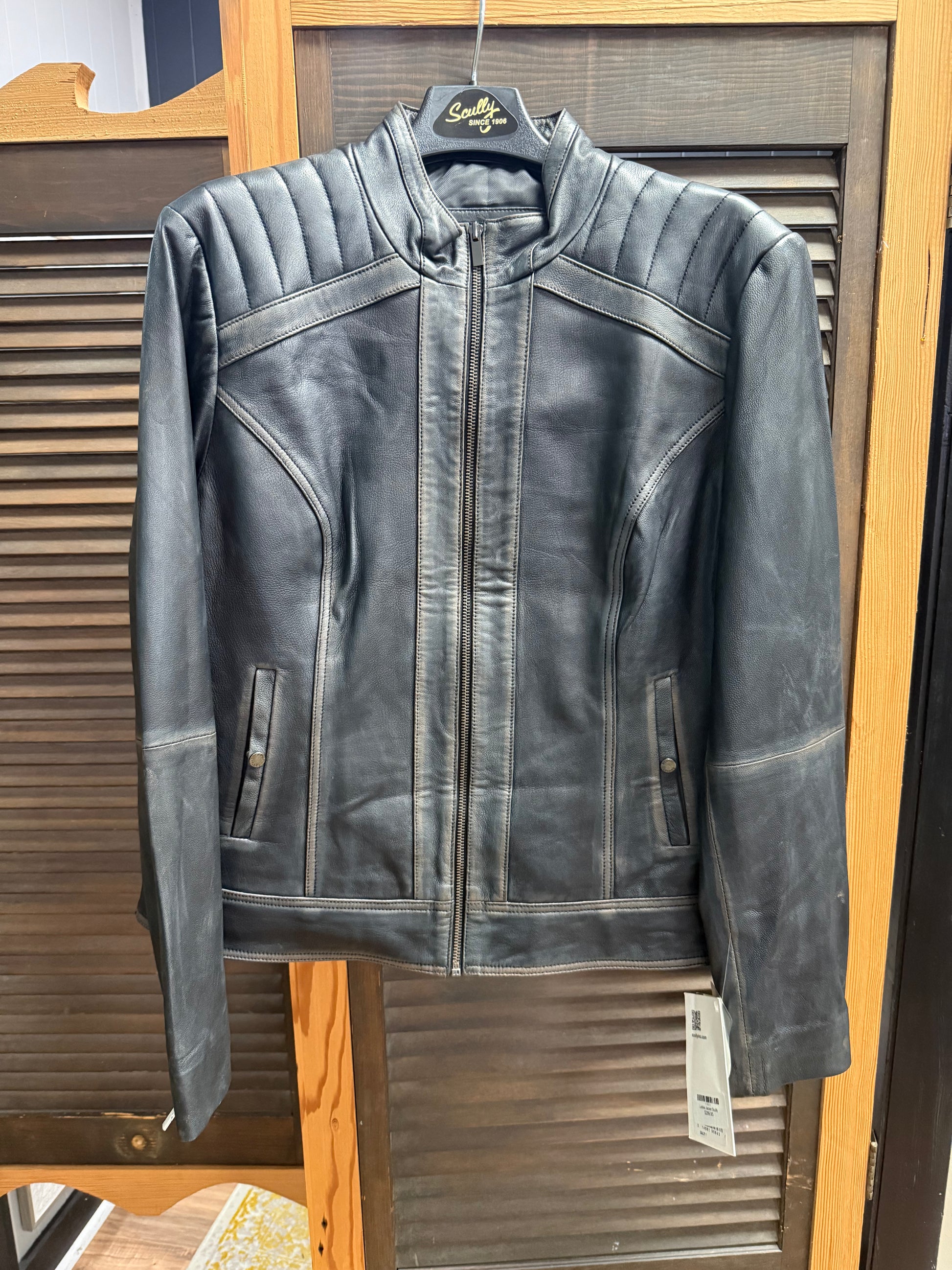 Black leather jacket on a hanger with a visible brand tag against a wooden background