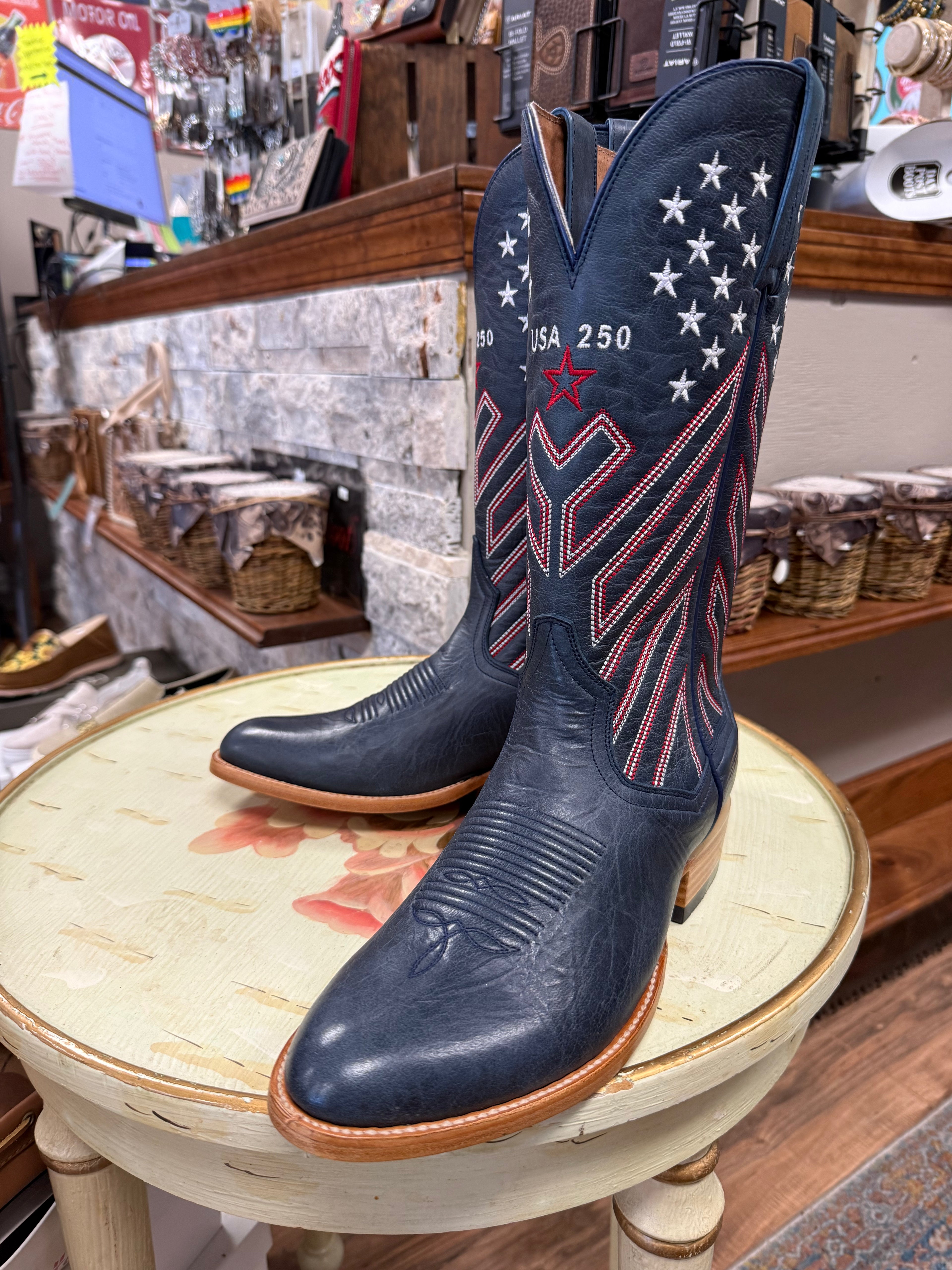 Navy blue cowboy boots with American flag design on a round table in a store setting.