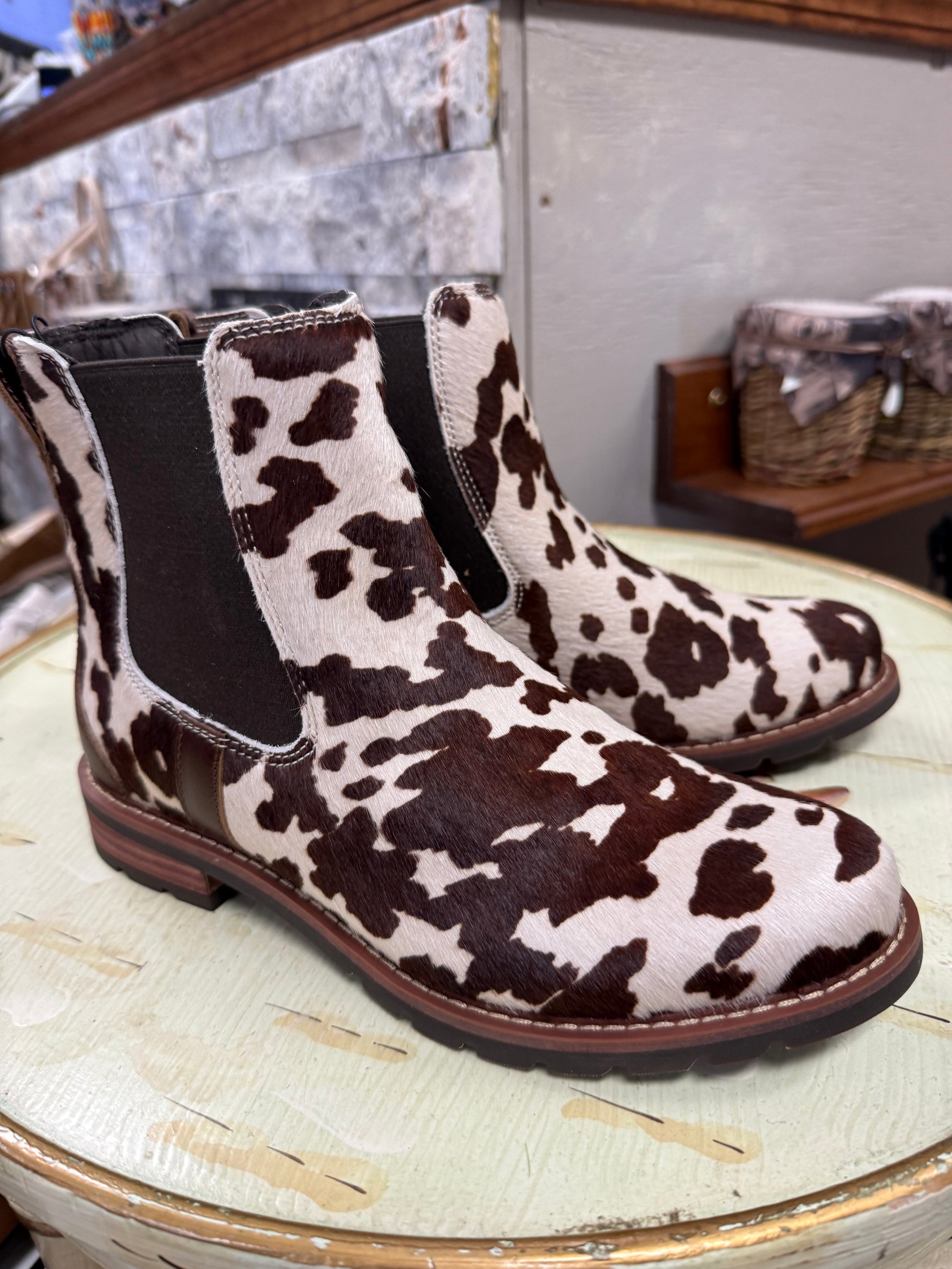 Cow print boots on a round wooden surface with a stone wall background