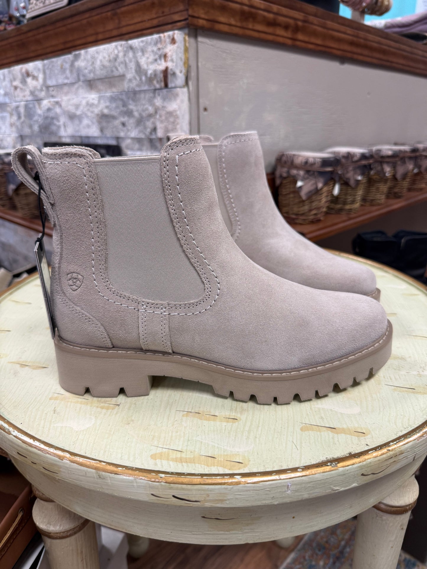 Pair of light gray boots on a round wooden stool with a store interior background.
