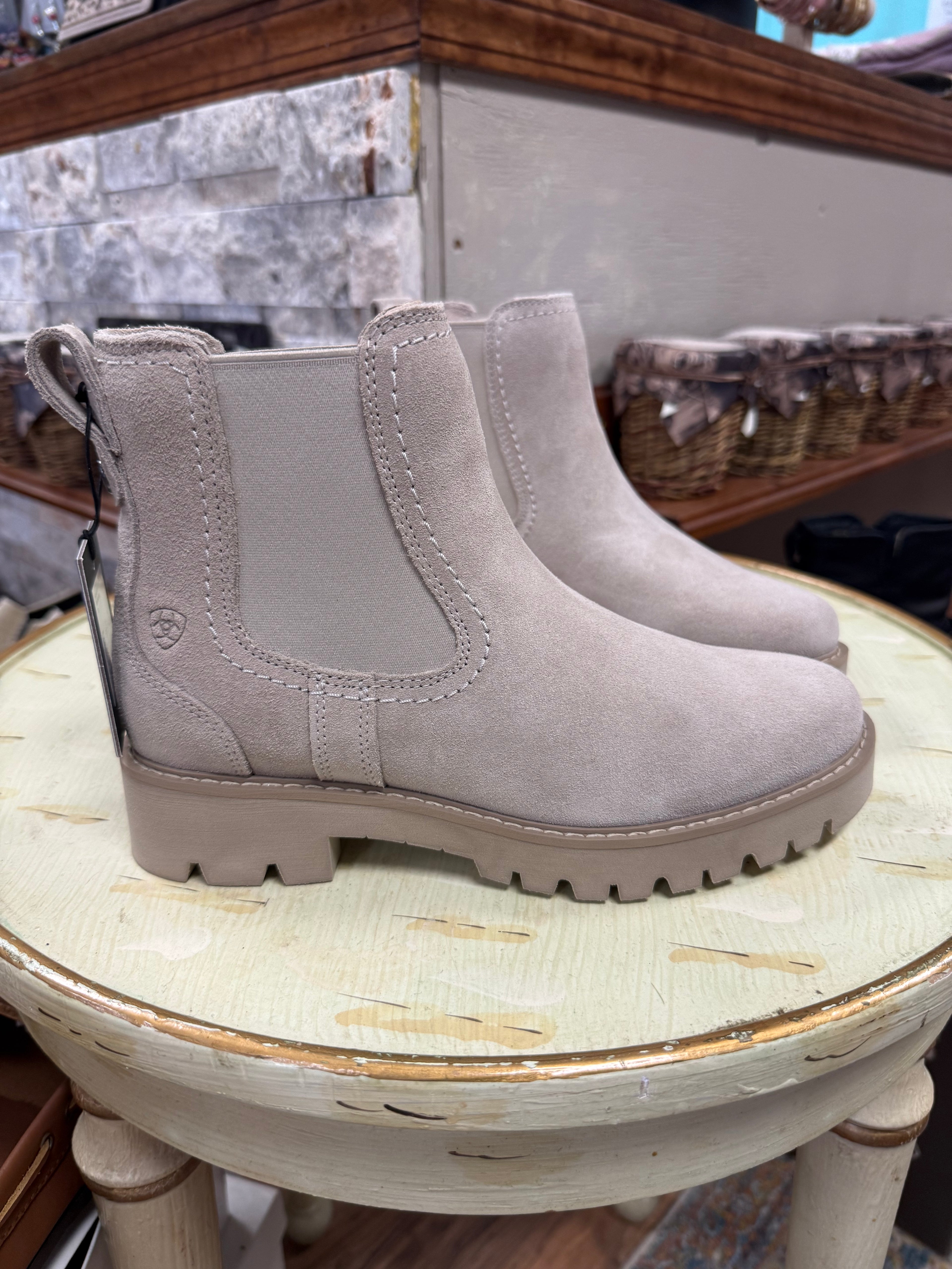 Pair of light gray boots on a round wooden stool with a store interior background.