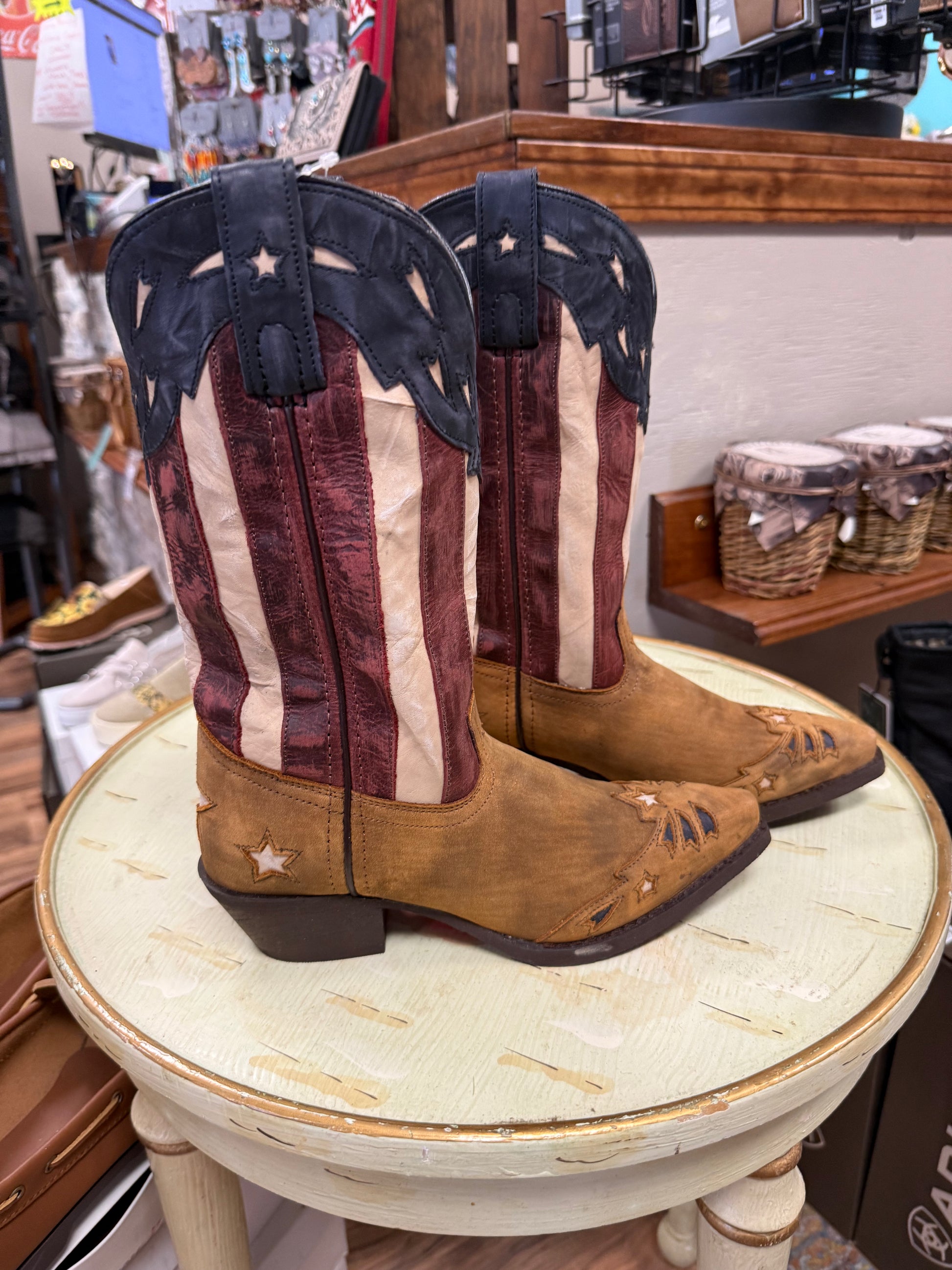 Pair of American flag-themed cowboy boots on a round table in a store setting.