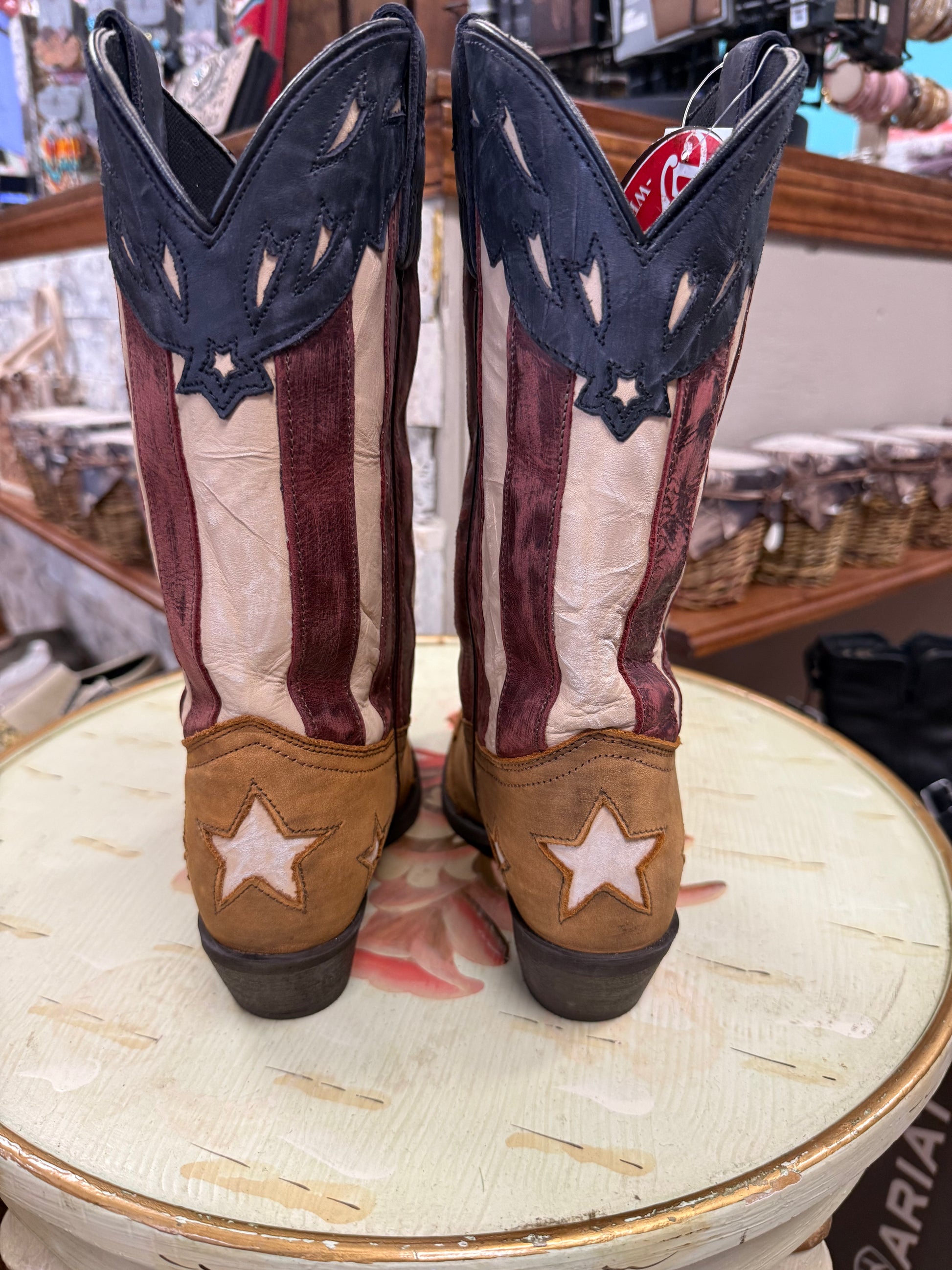 Pair of American flag-themed cowboy boots on a round surface with a blurred background.