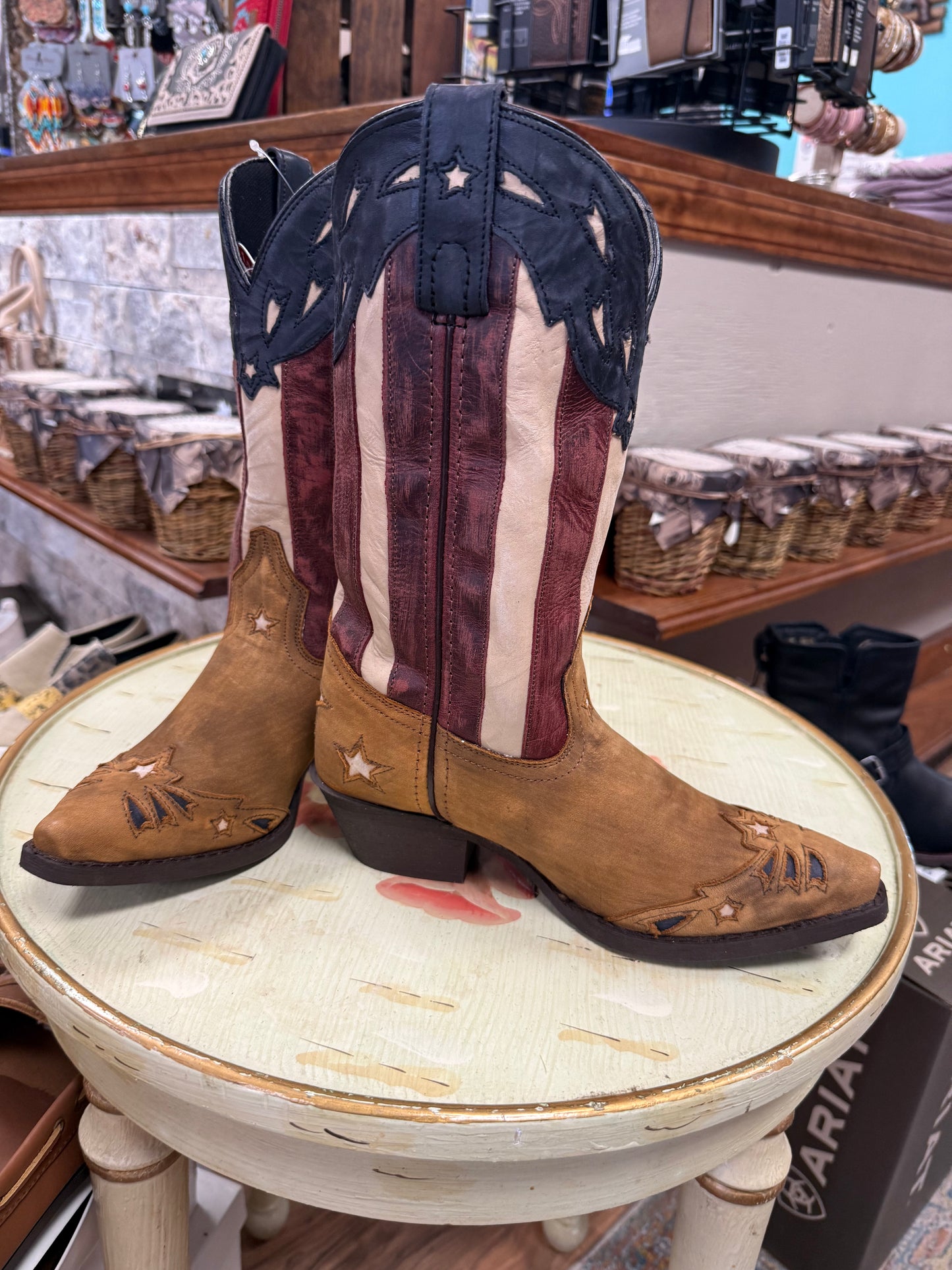 Pair of American flag cowboy boots on a round stool in a store setting.