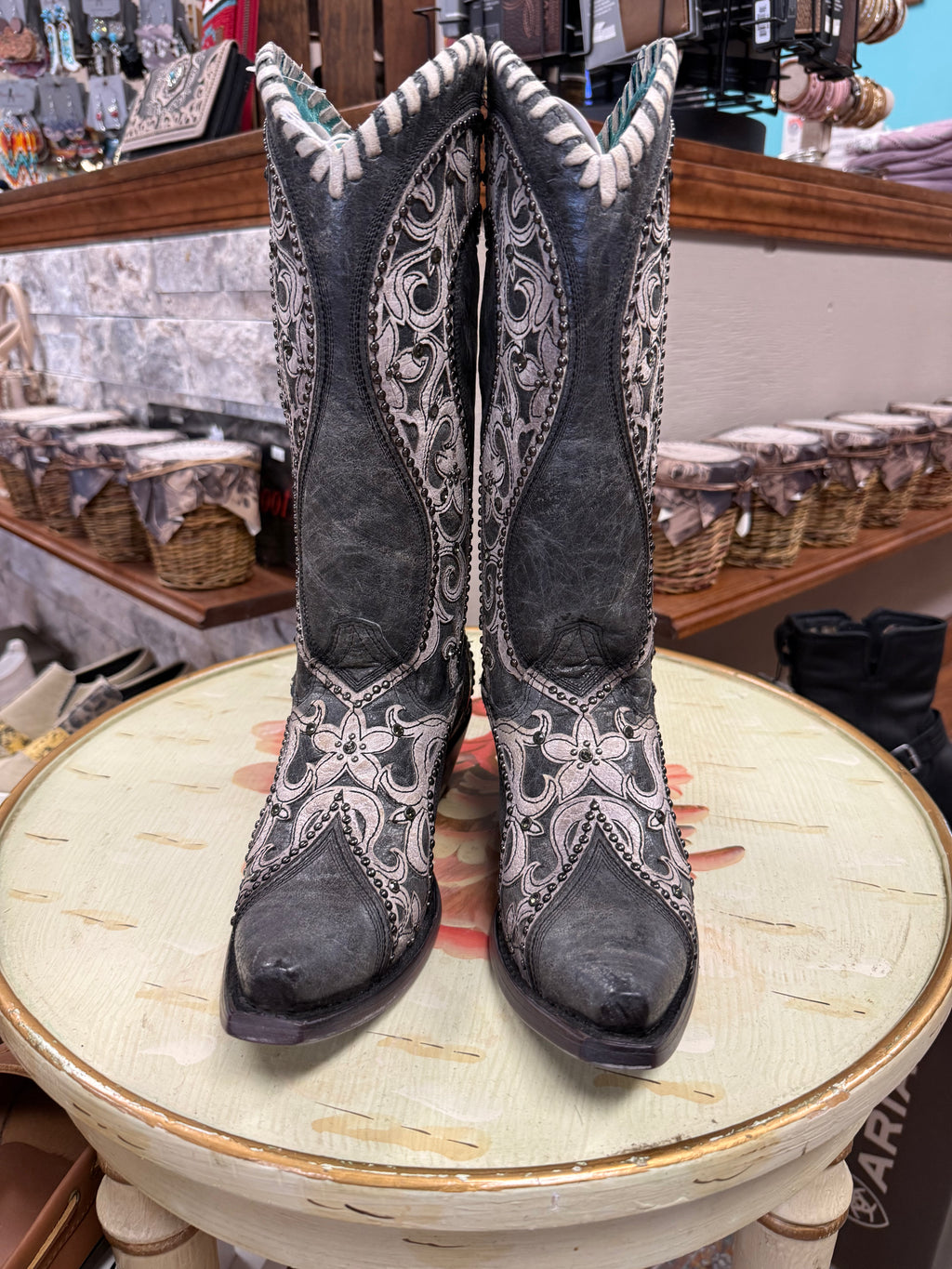 Pair of black cowboy boots with white patterns on a round table in a store setting.