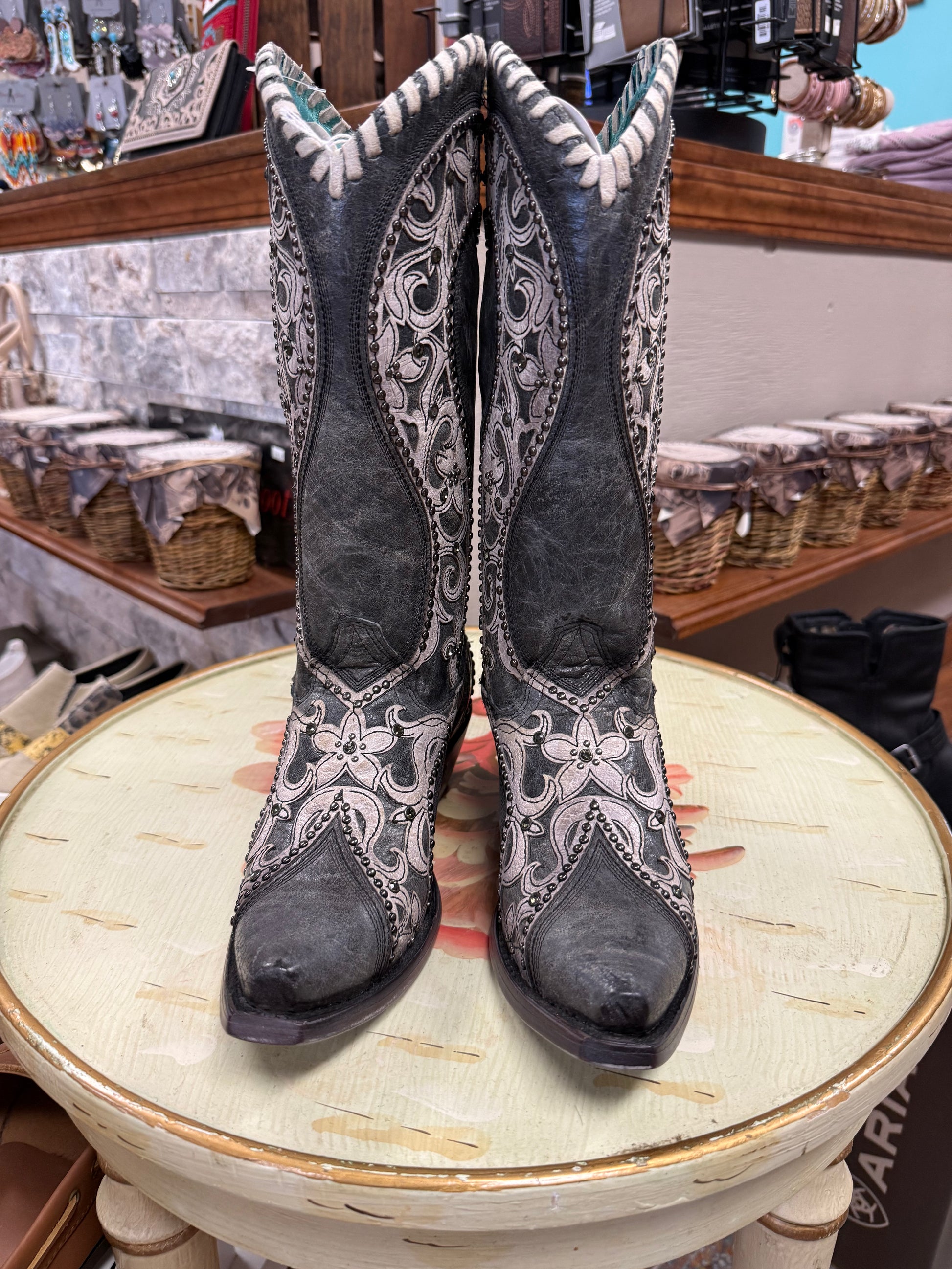Pair of black cowboy boots with white patterns on a round table in a store setting.