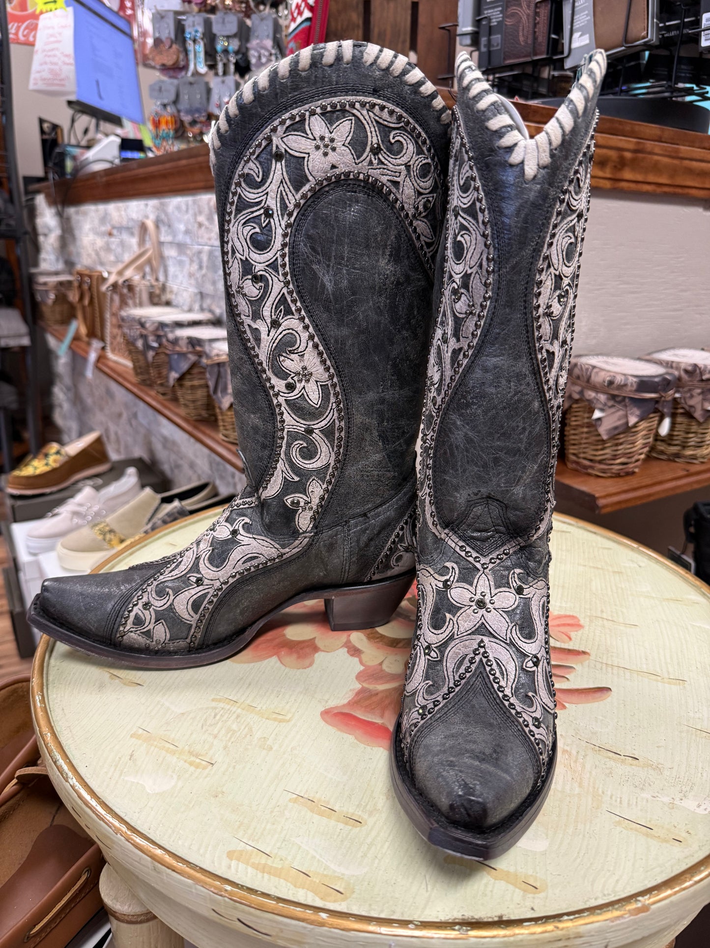 Pair of gray cowboy boots with intricate white patterns on a floral table.