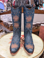 Pair of blue embroidered boots on a round table with a store setting in the background.
