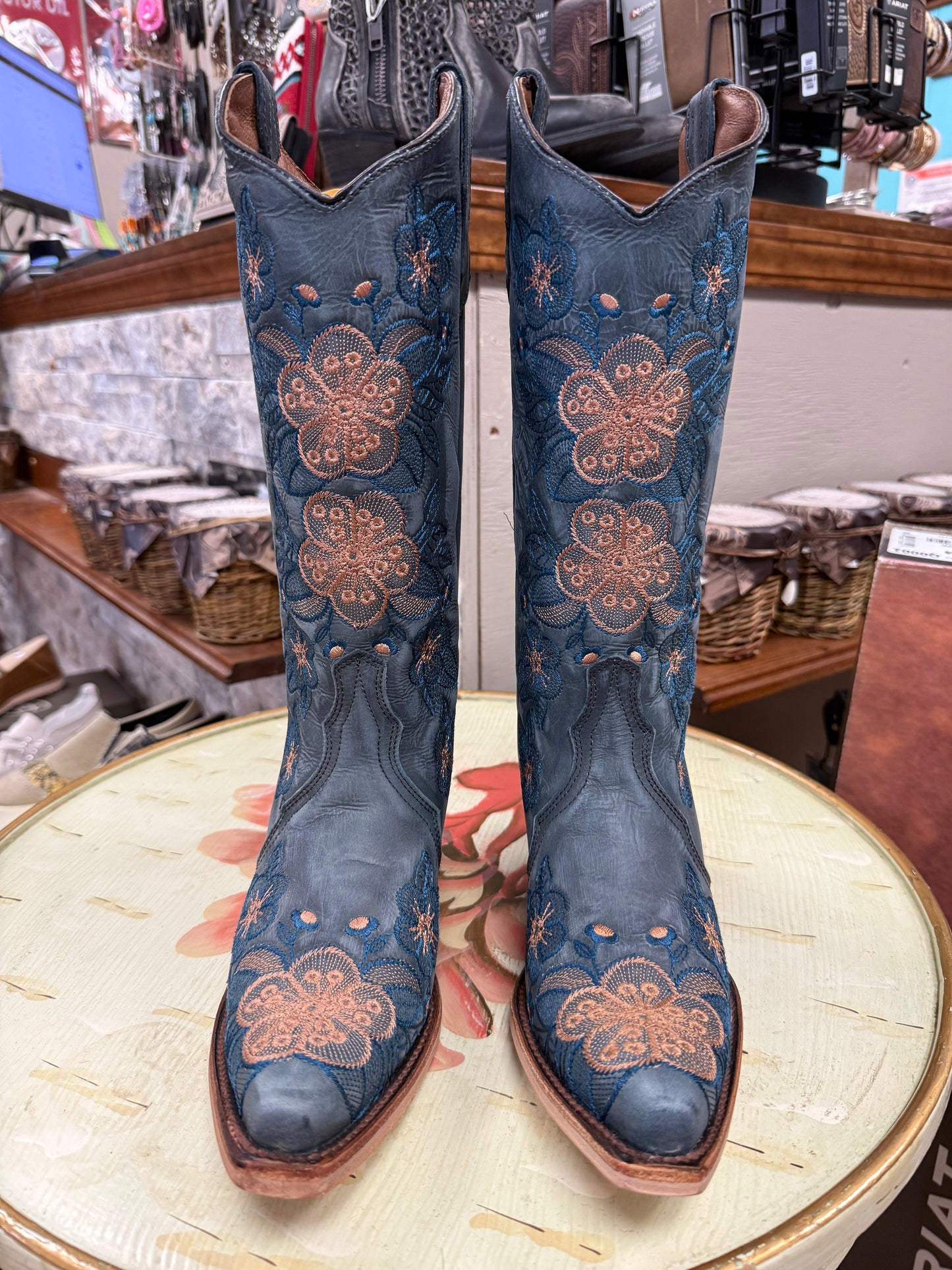 Pair of blue embroidered boots on a round table with a store setting in the background.