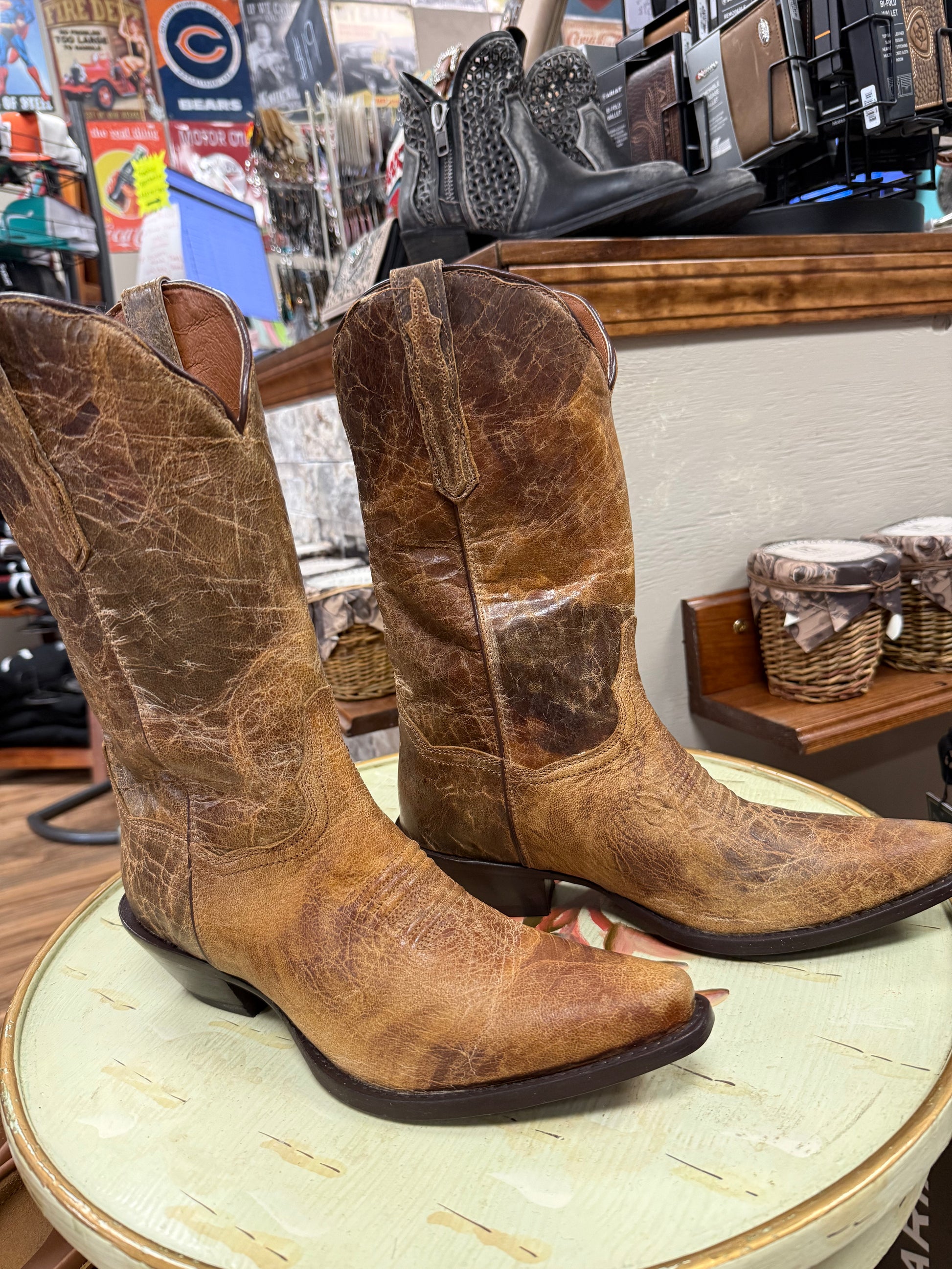 Pair of brown leather cowboy boots on a round table in a store setting.