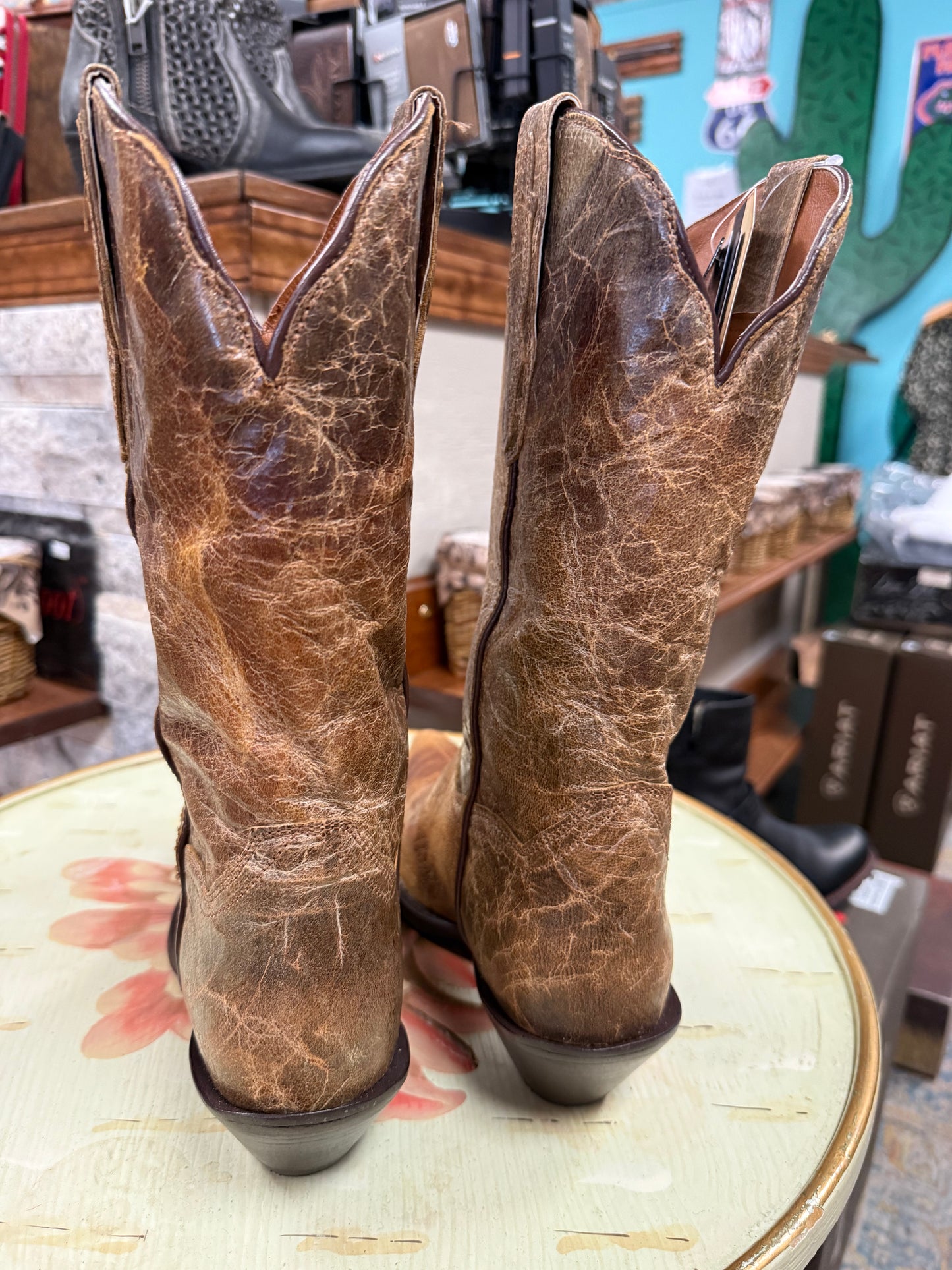 Pair of brown leather cowboy boots on a table with a store setting in the background